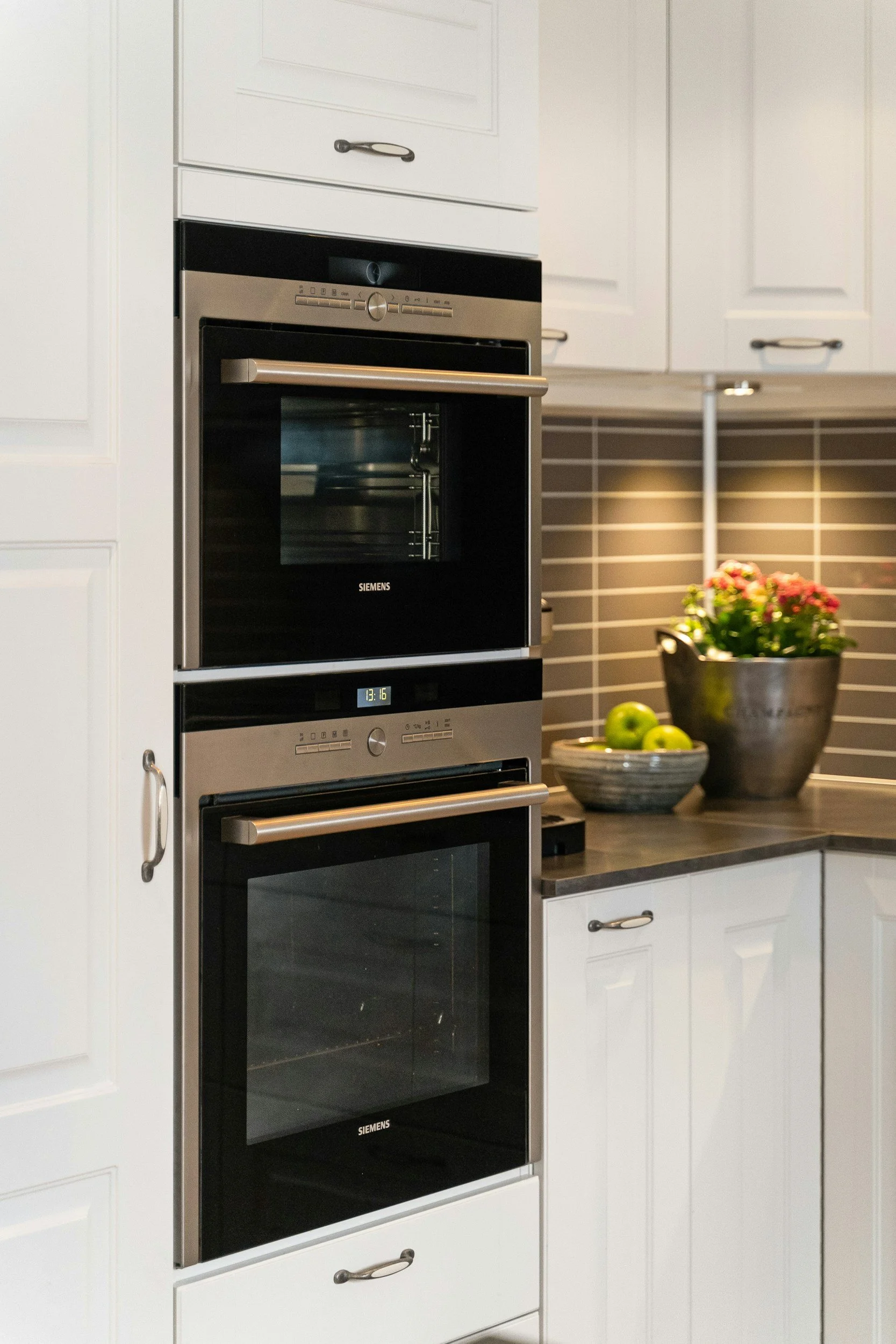 Kitchen with built-in Siemens oven, white cabinets, gray countertop, and flowers in a pot on the counter.