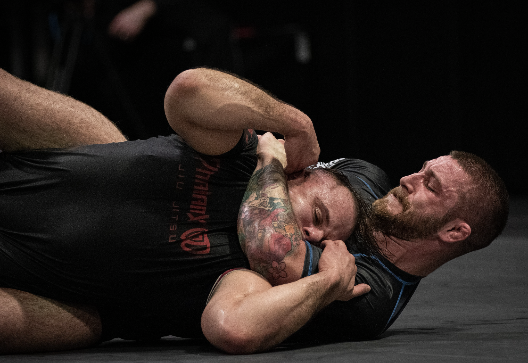 Two male athletes grappling and struggling on the mat during a wrestling match, with one pinning the other.