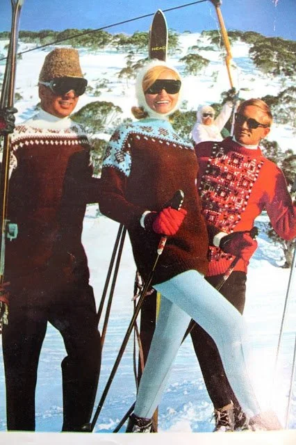 Three people in winter clothes and sunglasses posing with skis on a snowy mountain.