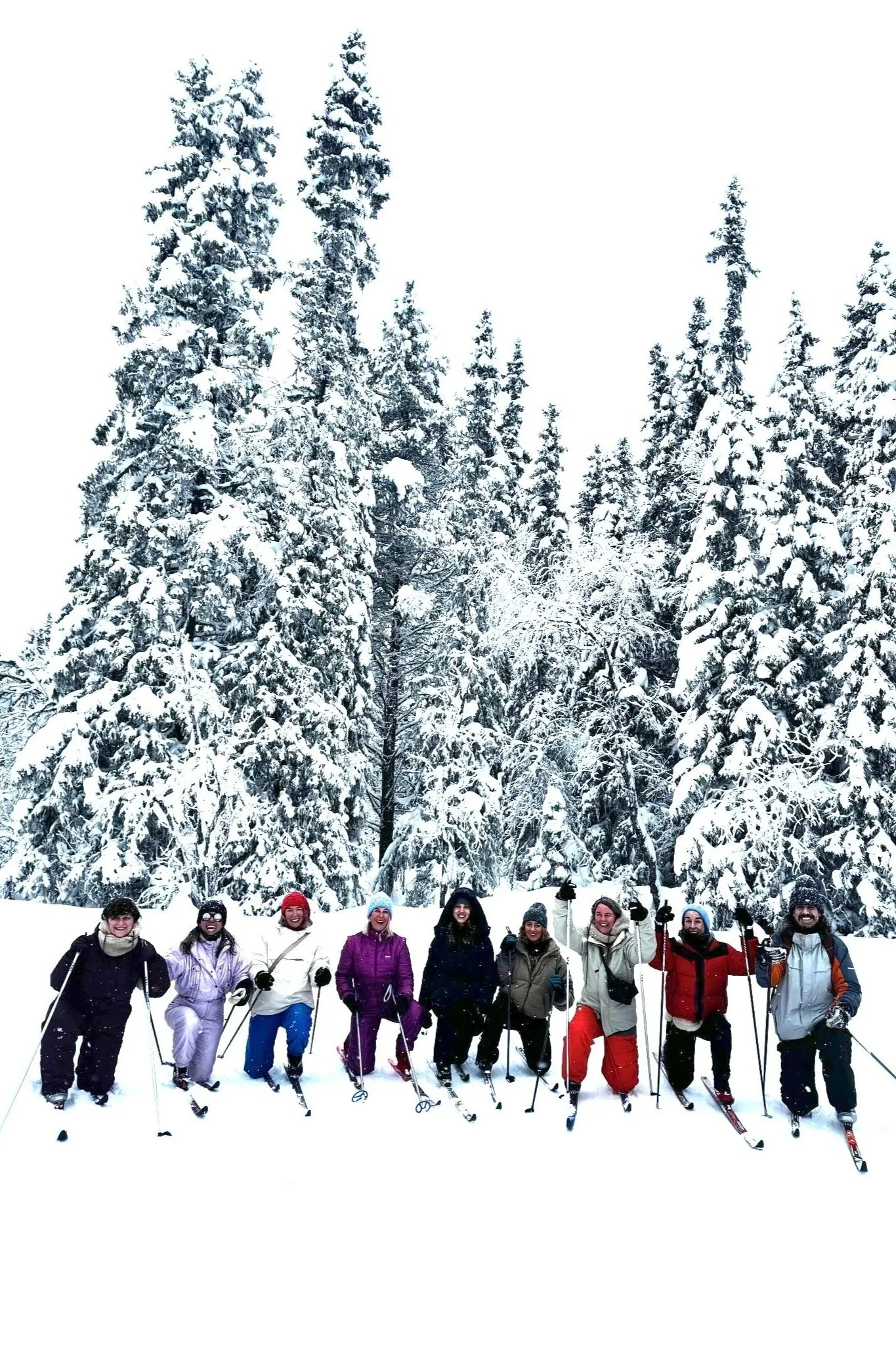 Group of people in winter clothing standing in snow with trees covered in snow in the background.