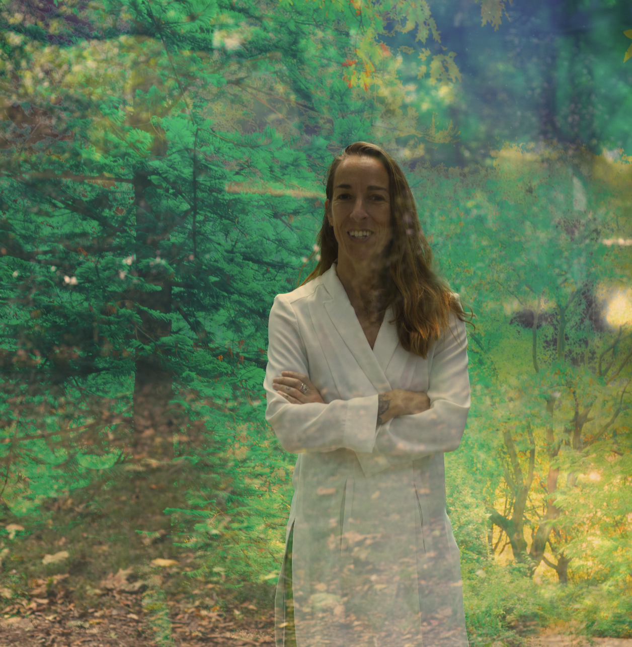 A woman in a white coat standing in front of a large digital or printed image of a forest with green trees and sunlight.