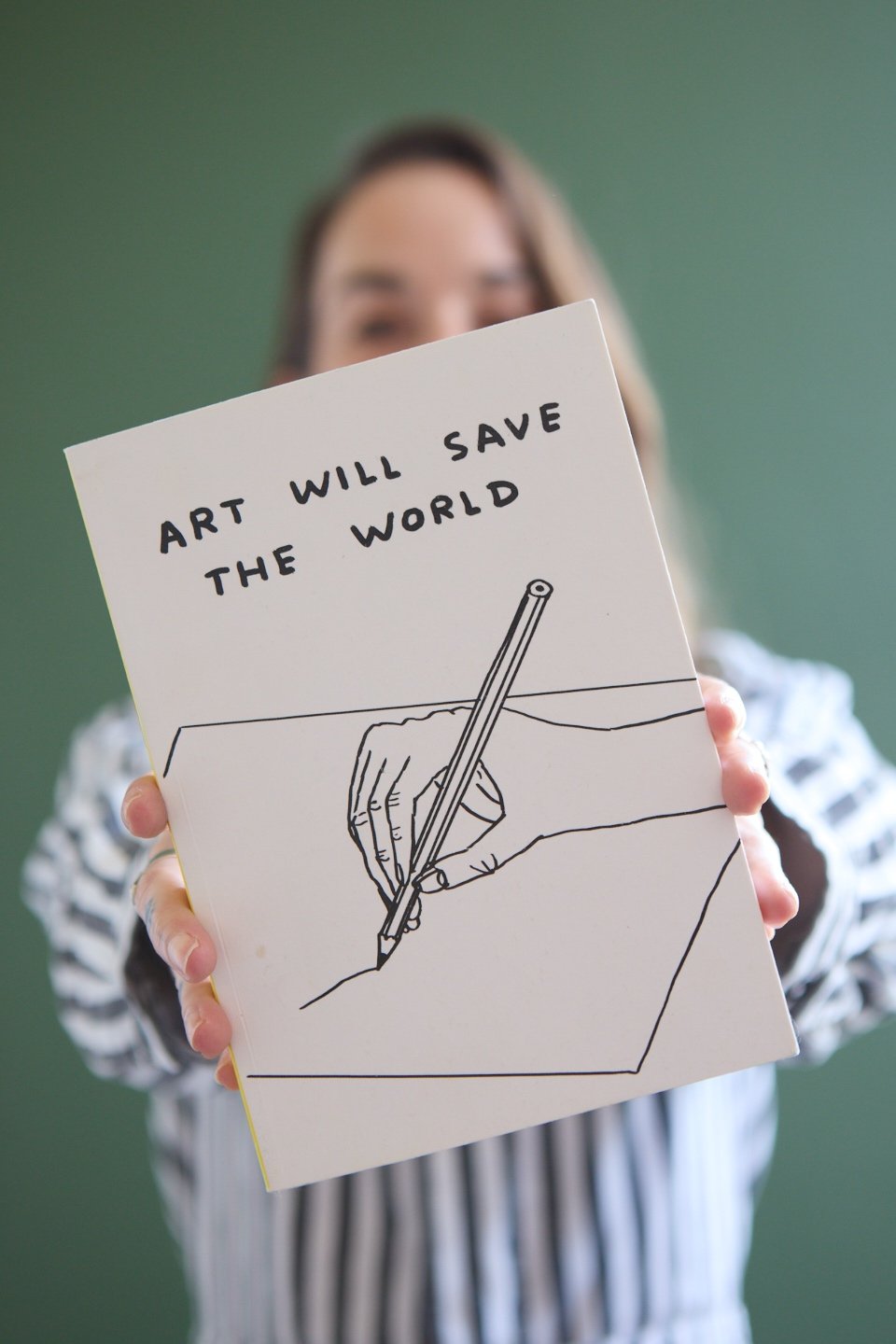 Woman holding a sign with a drawing of a hand and pencil, and the text "Art will save the world"