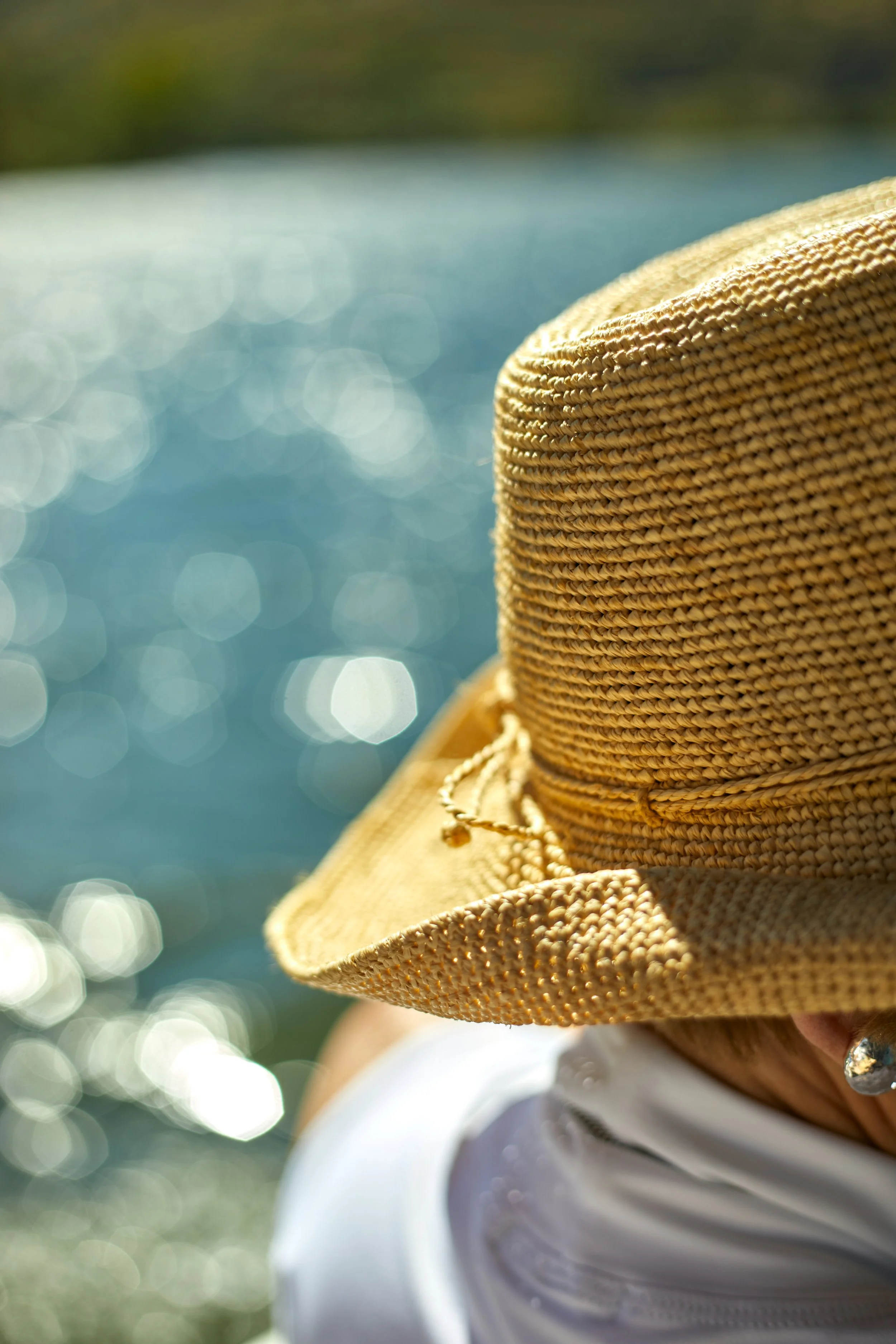 A person wearing a wide-brimmed straw hat near a body of water that is reflecting sunlight.