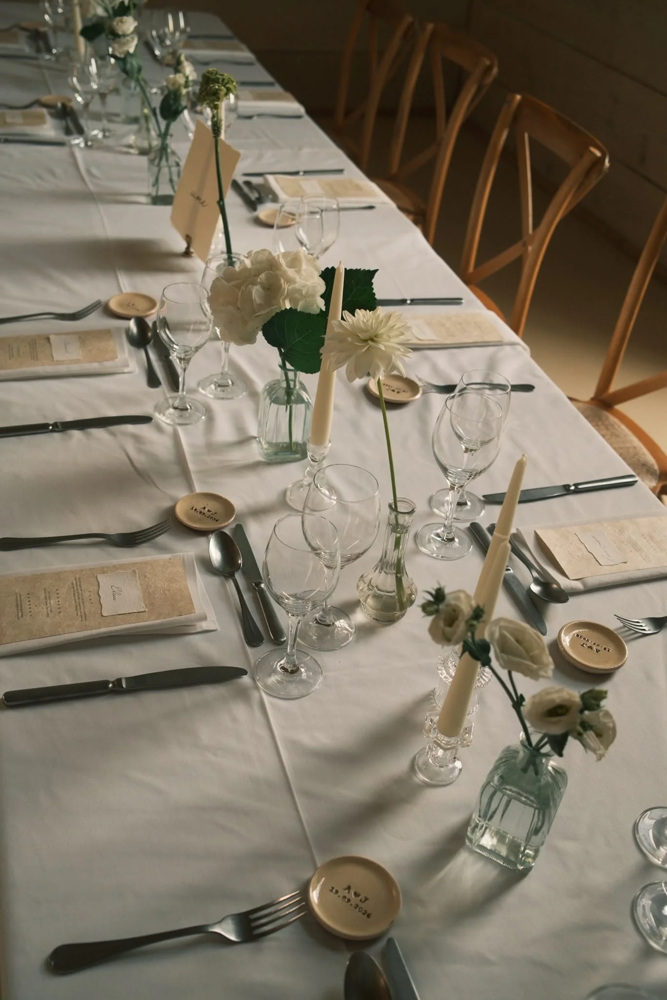 Table de mariage élégamment dressée avec des vases de fleurs blanches, des bougies, des verres à vin, des assiettes et des couverts en métal.