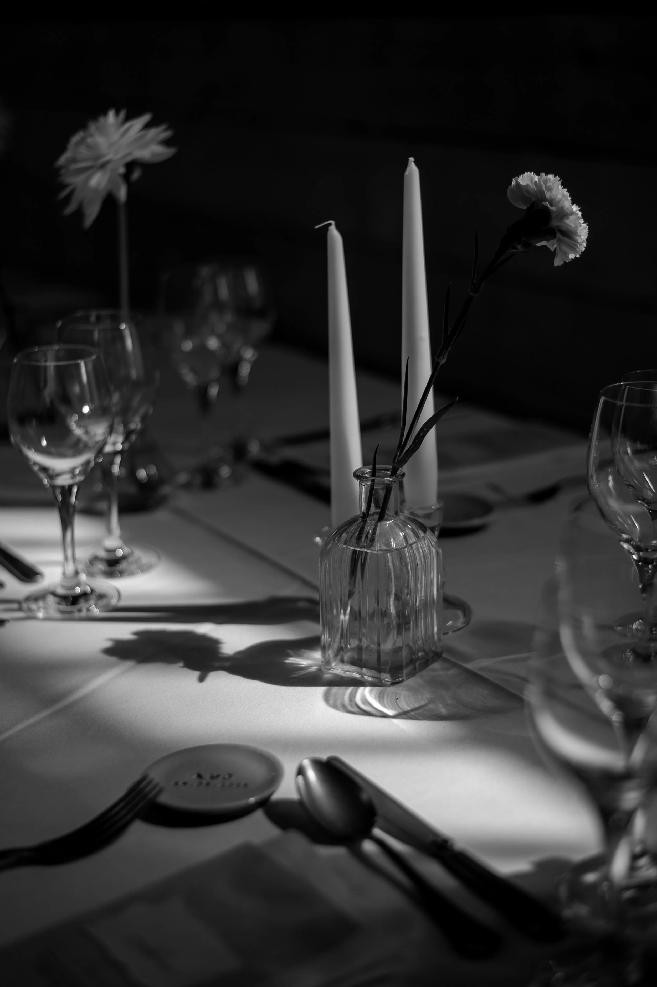 Une table de dîner avec des verres, des bougies blanches, et des fleurs dans des vases en verre, éclairée doucement pour une ambiance élégante.