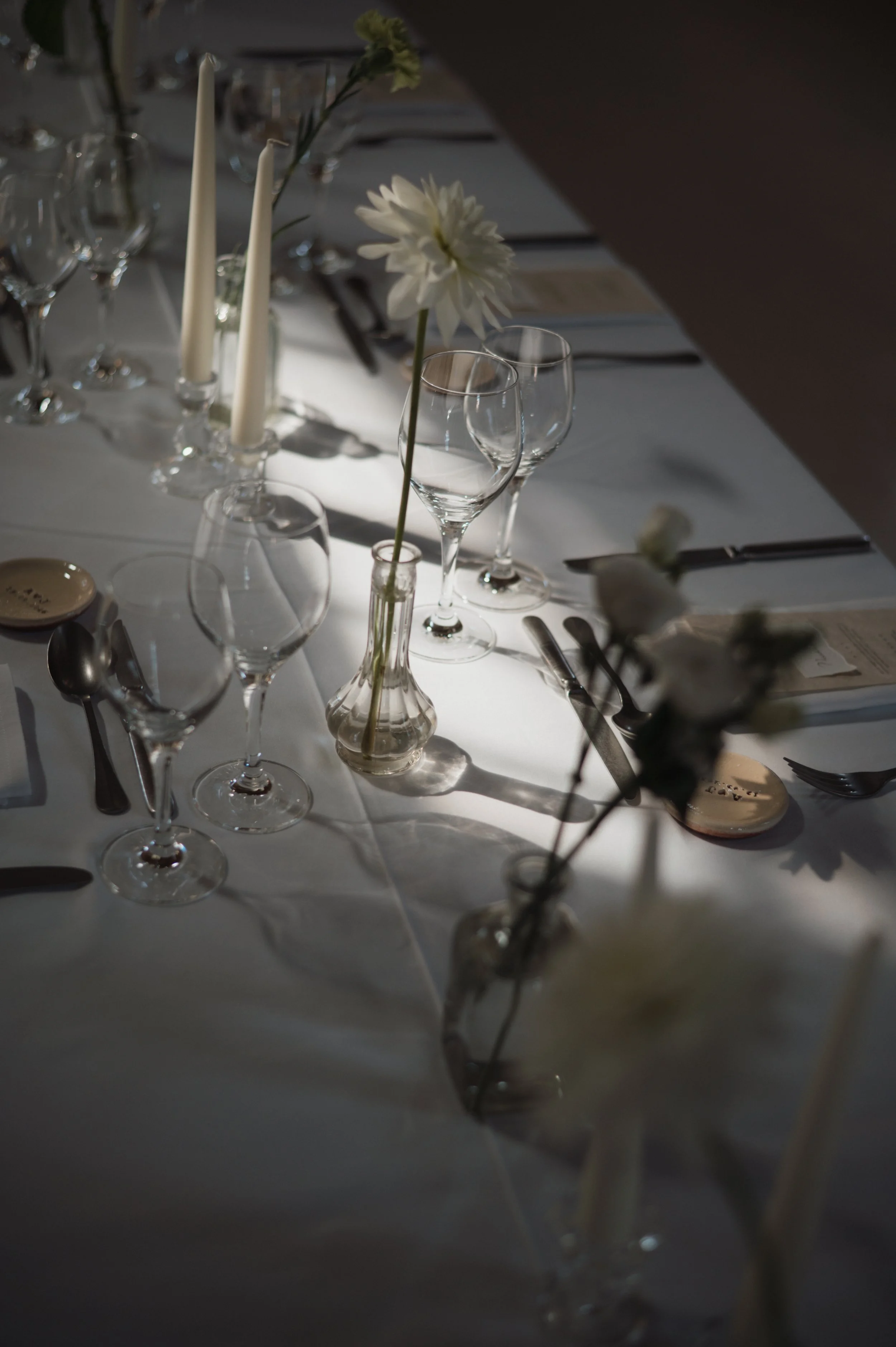 Table dressée avec des verres à vin, des assiettes et des couverts, décorée de fleurs blanches dans des vases, dans un éclairage tamisé, pour un repas élégant.