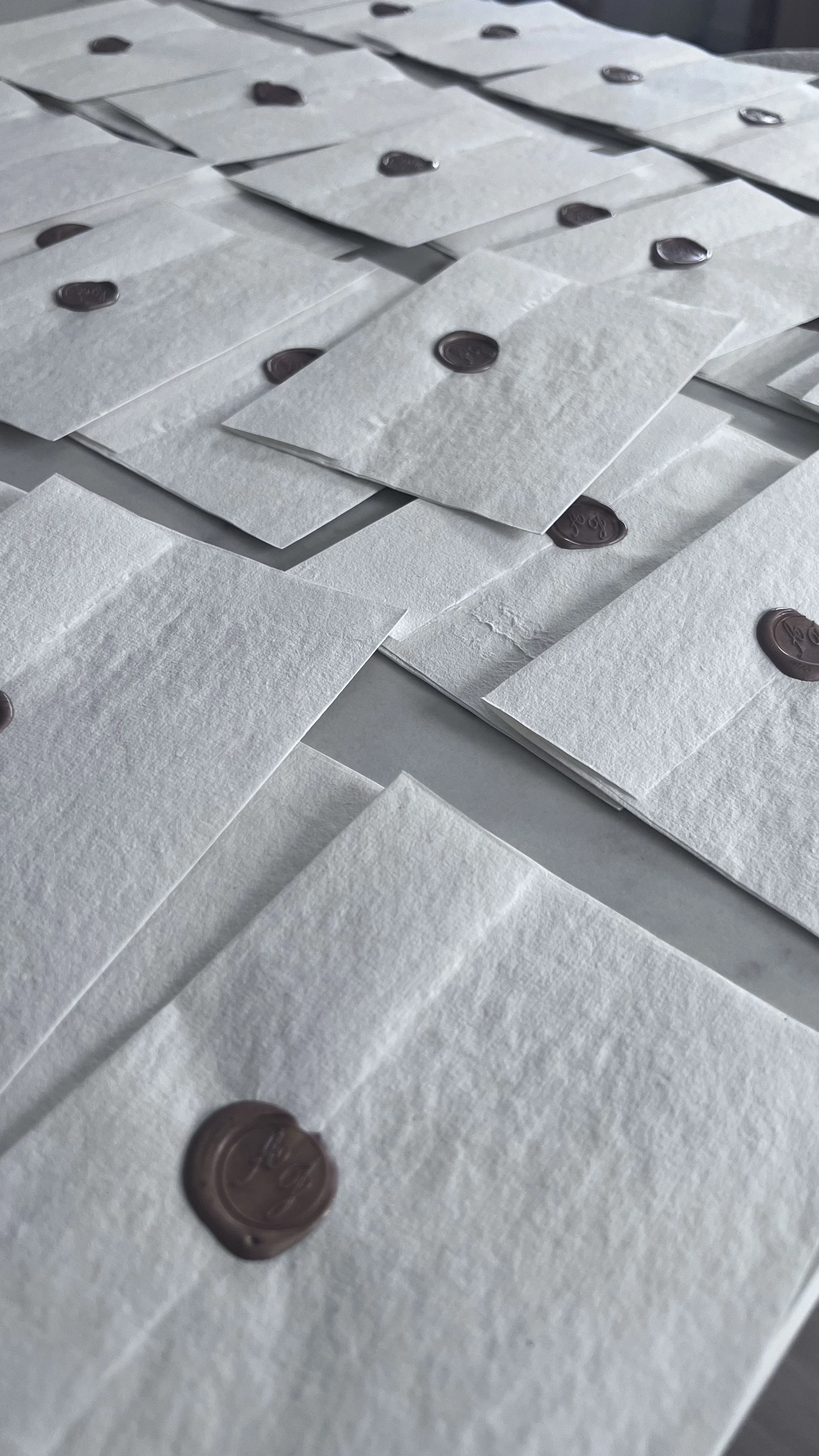 Enveloppes blanches avec un cachet en cire rouge foncé, disposées en rangées sur une surface plane.