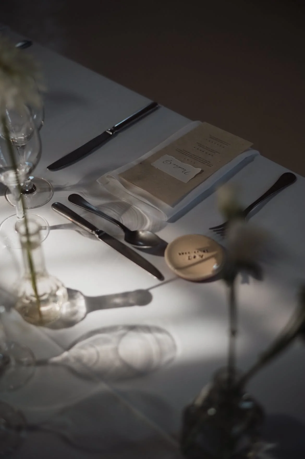 Une table de dîner élégante avec une nappe blanche, des couverts en argent, des verres à vin et un menu placé au centre.