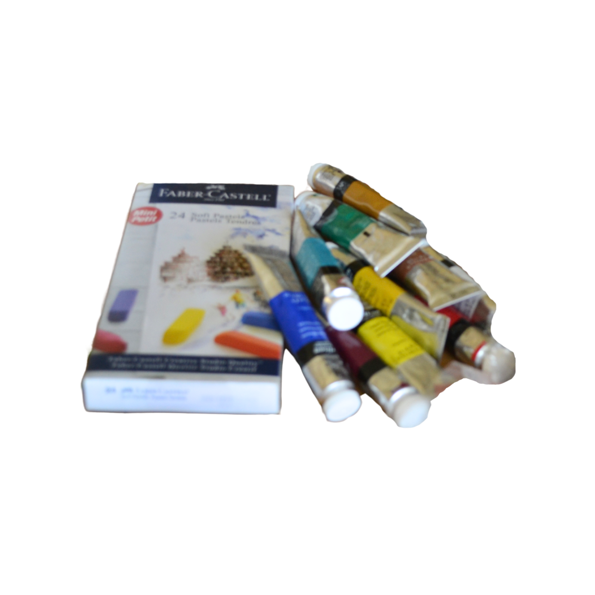 A partially visible box of Faber-Castell watercolor paints and several paint tubes spread out on a surface.