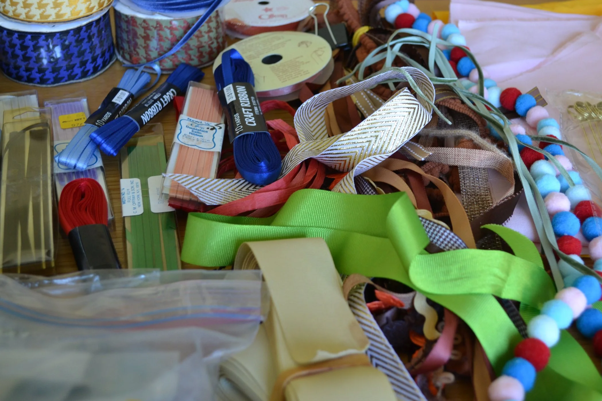 Assorted craft supplies including ribbons, pom-pom strings, and fabric around a table.