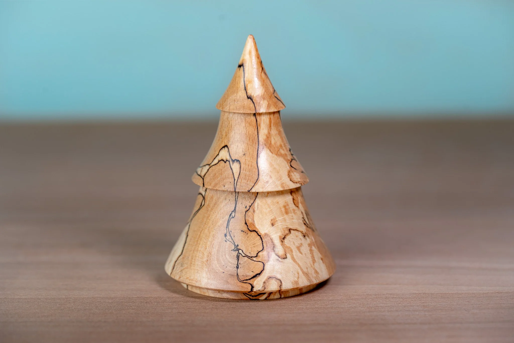 A small tree-shaped sculpture made of light-colored wood with dark grain patterns, placed on a flat surface with a plain blue background.