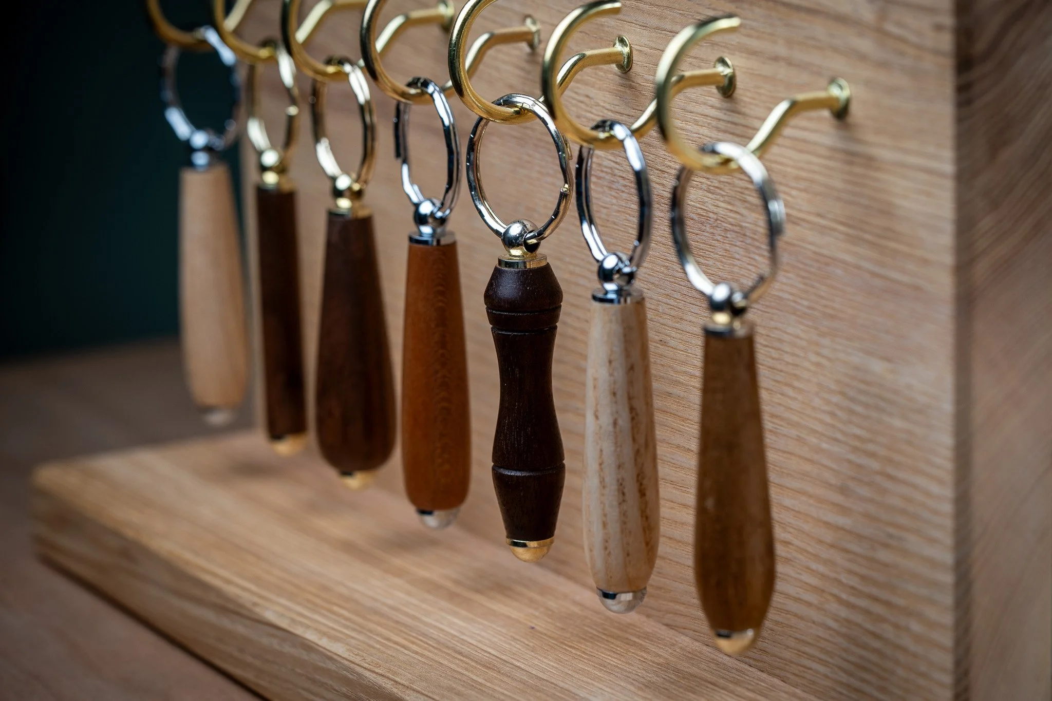 A display board with multiple hooks, each holding different styles of small handled knives or carving tools, mounted on a wooden surface.