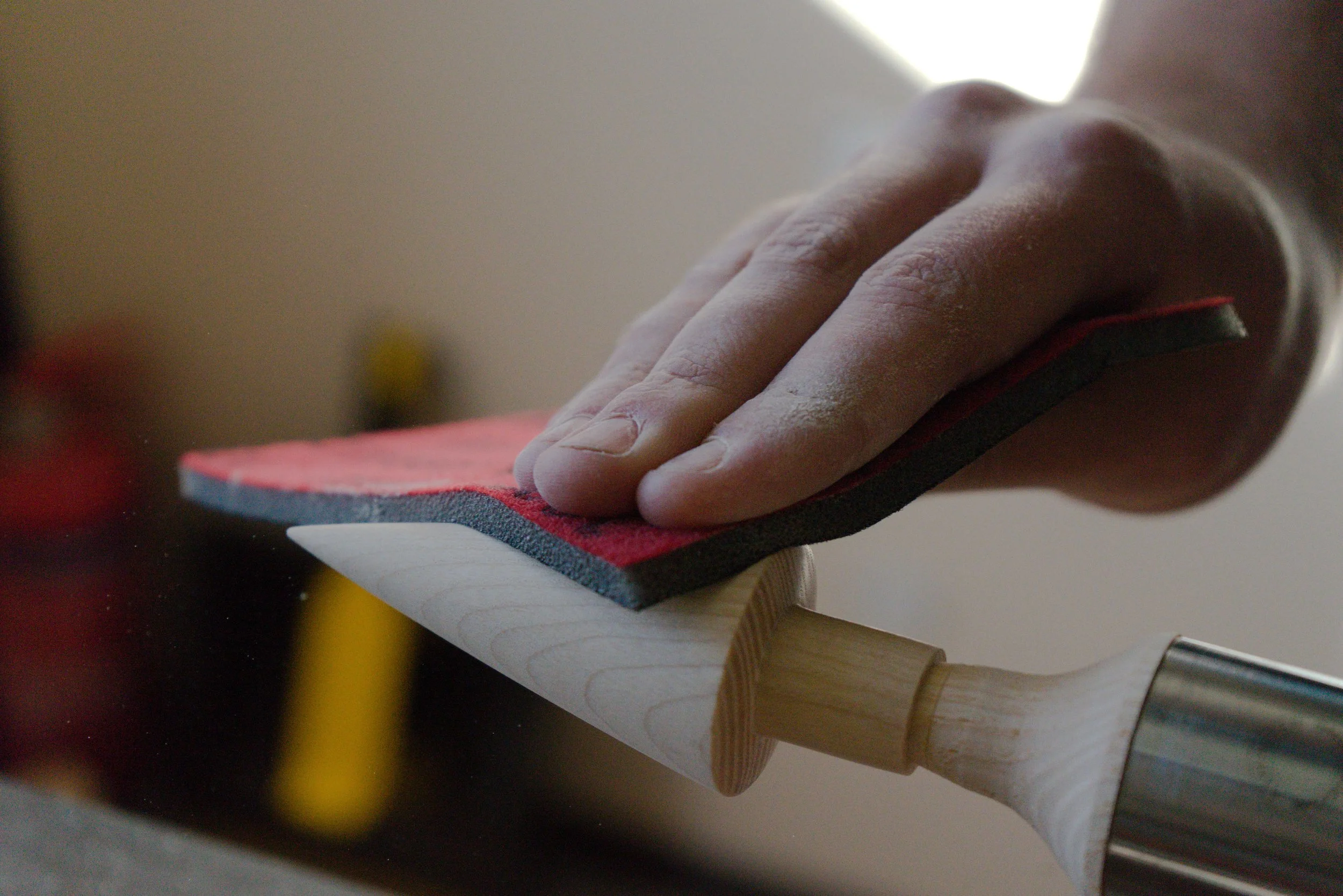 Close-up of a hand sanding a wooden piece on a workbench with a sanding pad, with dust particles visible in the air.