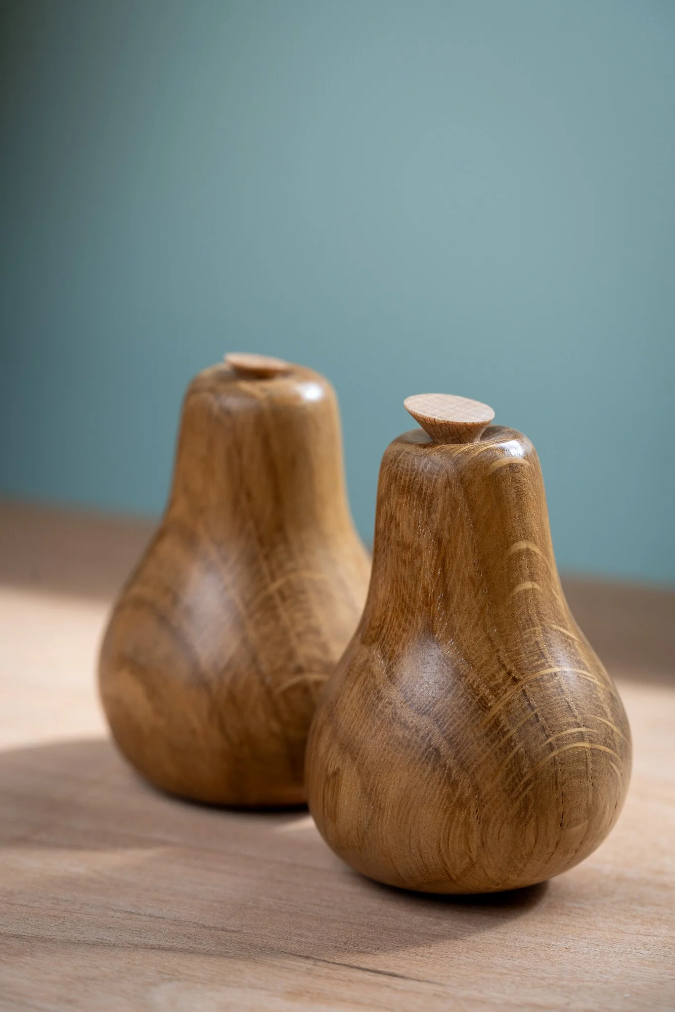 Three wooden objects with rounded bases and elongated bodies, each topped with a small, rounded, flat piece, placed on a wooden surface against a teal background.