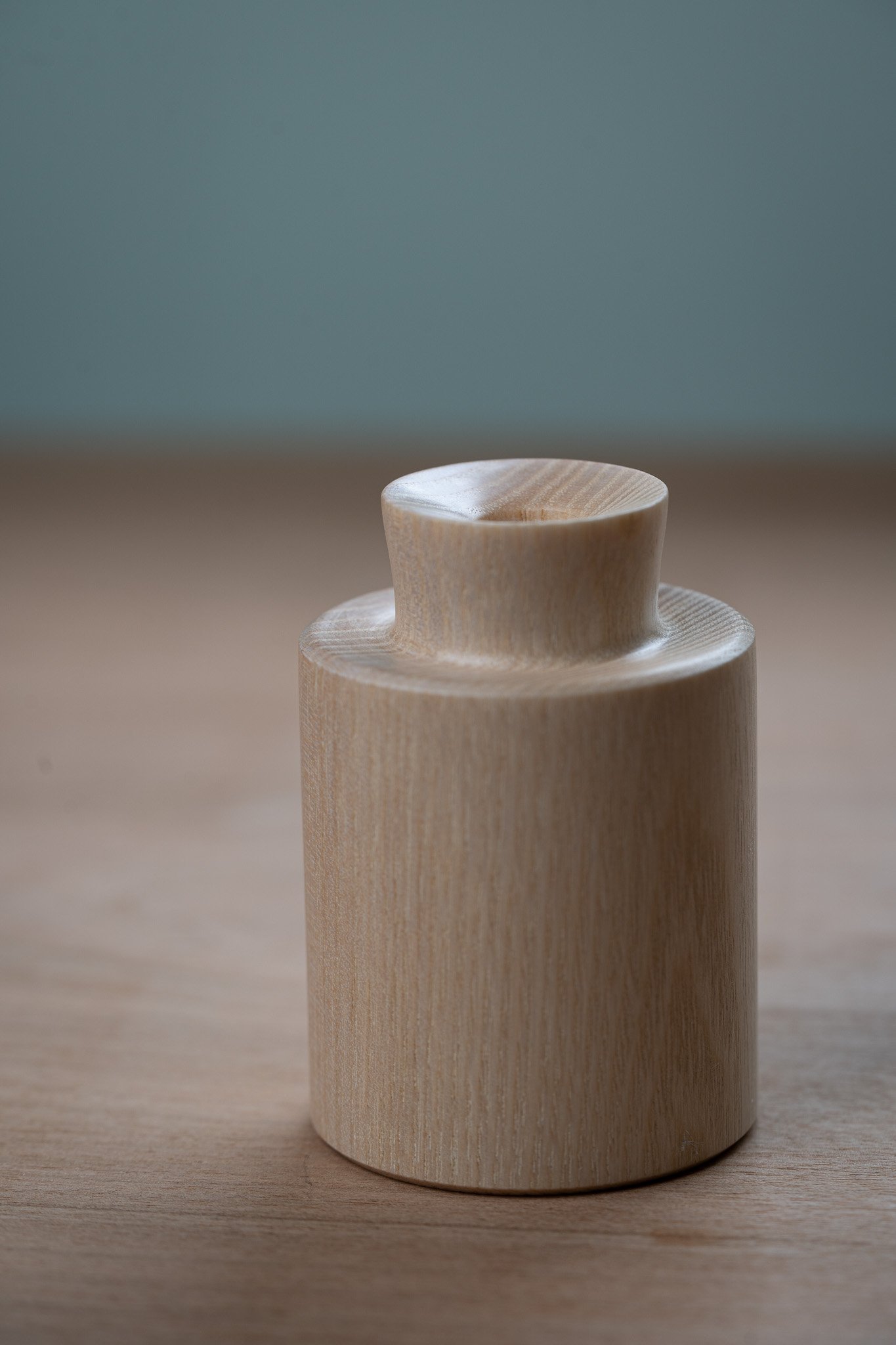 Close-up of a wooden cylindrical object with a rounded top, placed on a wooden surface with a blurred background.