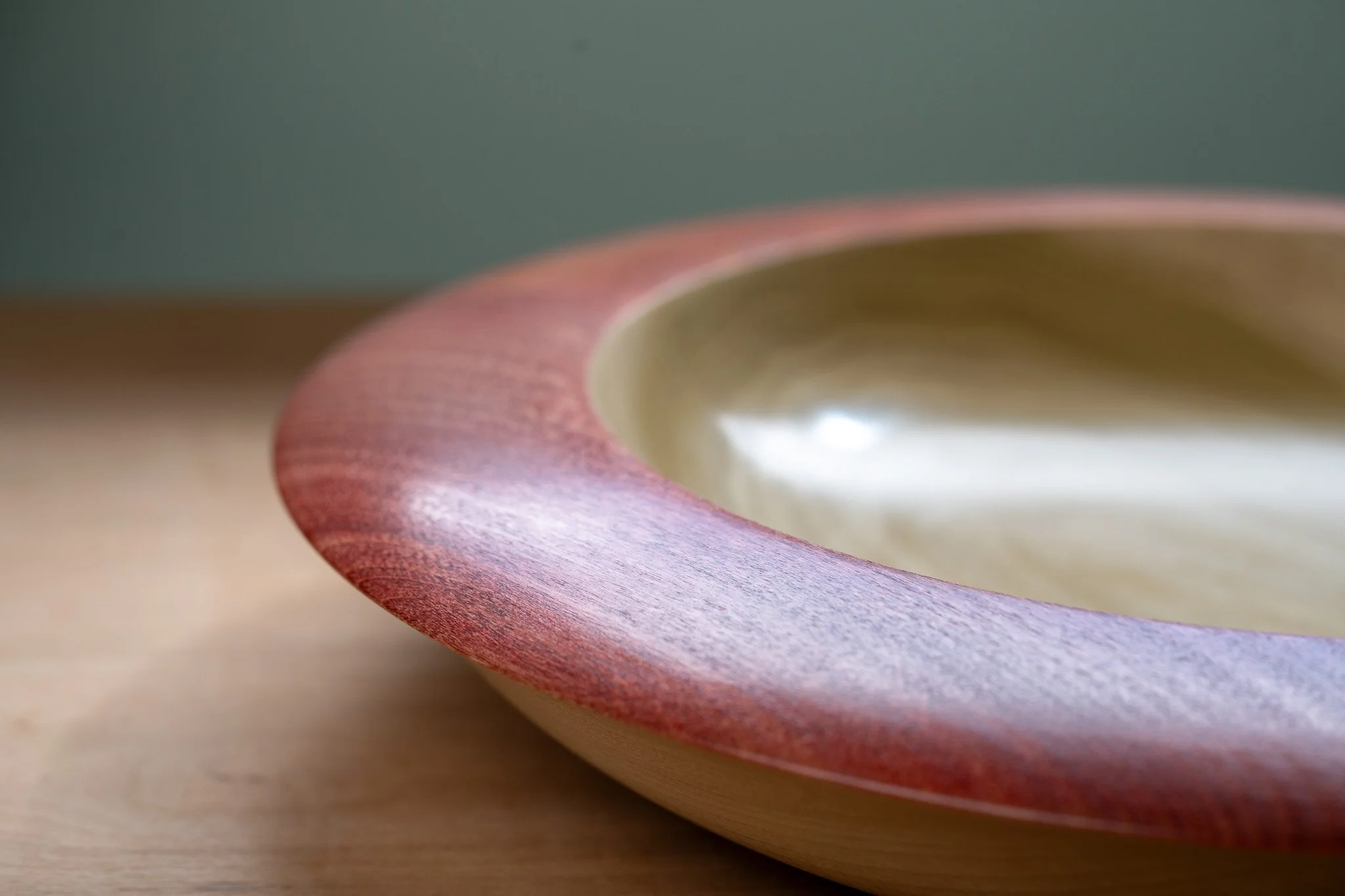 Close-up of a wooden plate with a curved edge and a bowl with a shiny interior, on a wooden surface.