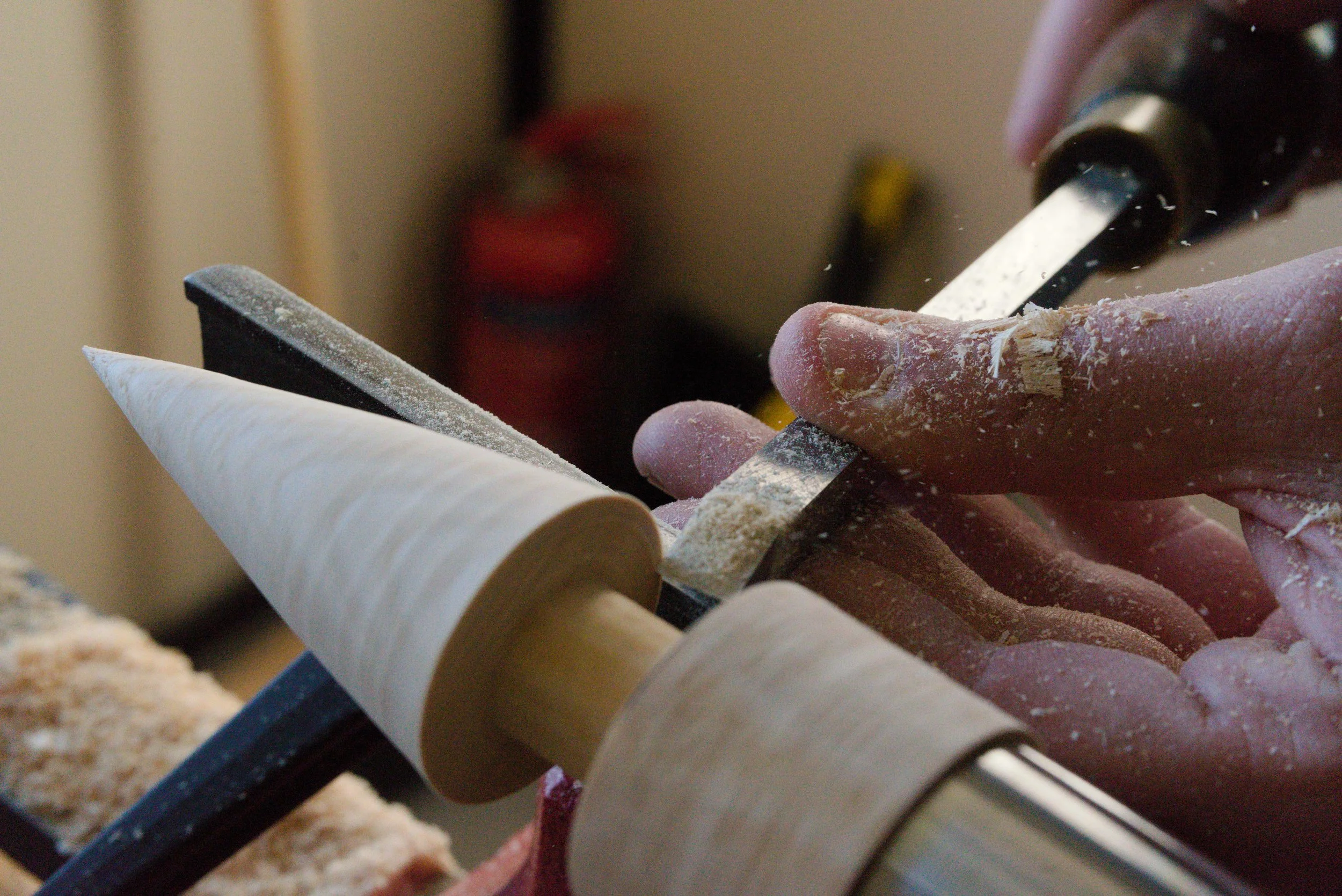 Close-up of a hand holding a wood carving chisel among partially carved wooden pieces.