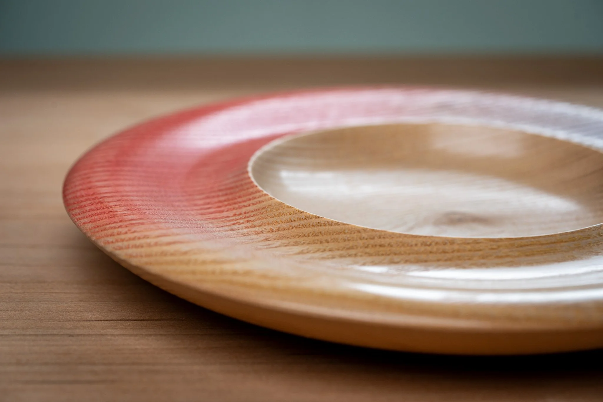 Close-up of a round wooden object with a carved pink and white design, resting on a wooden surface.
