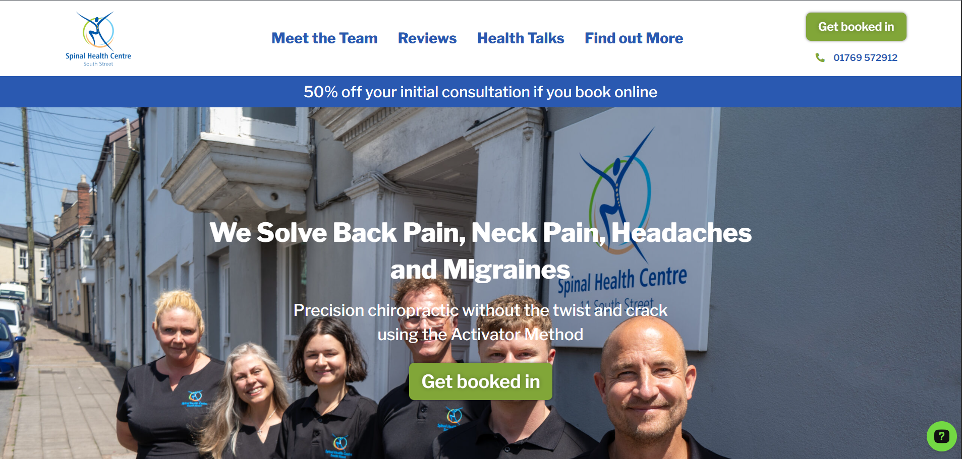 Group of smiling staff members standing outside the Spinal Health Centre on a sunny day, with the clinic's sign on the building behind them.