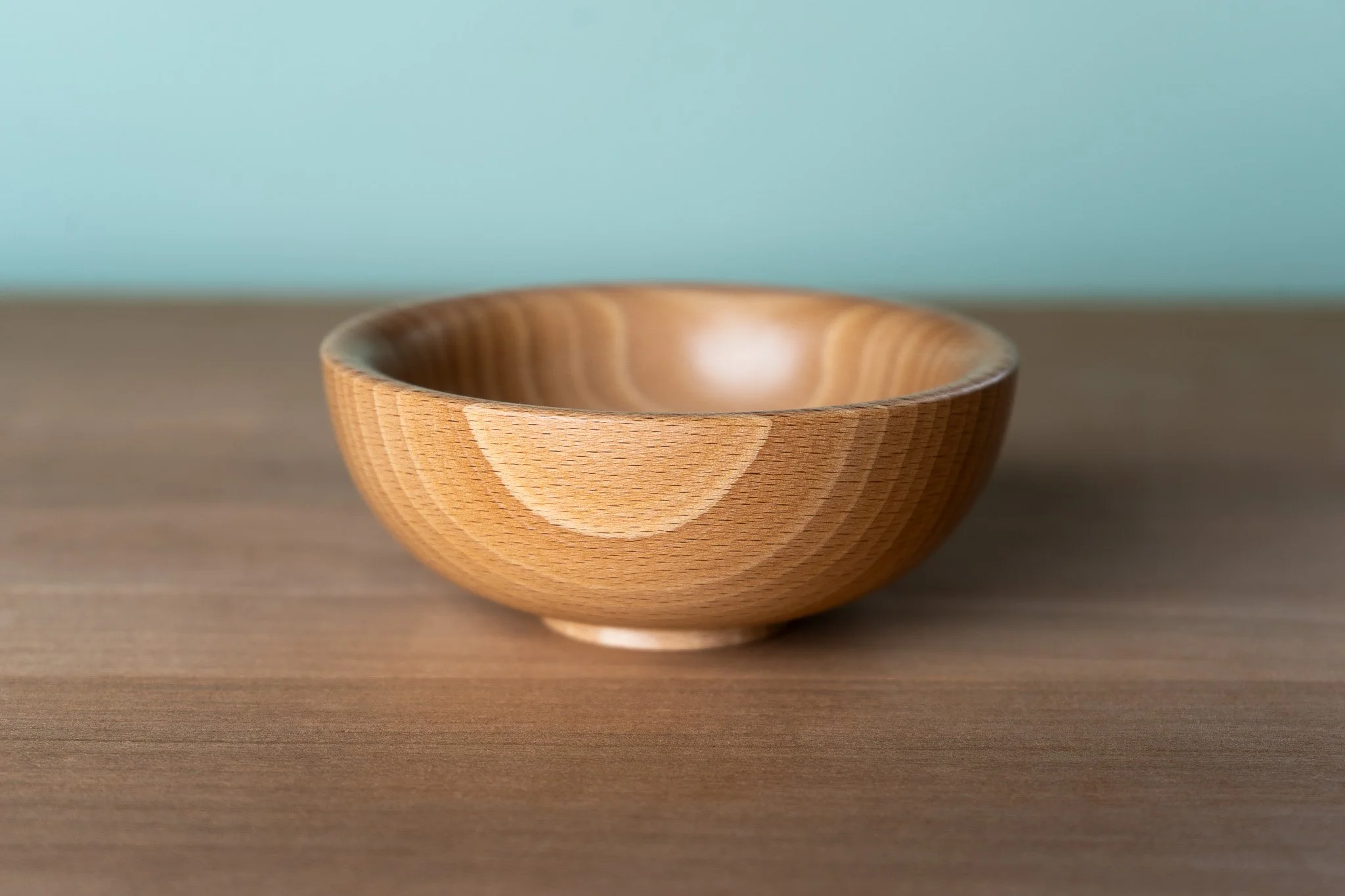 A wooden bowl is placed on a wooden surface with a plain, light blue background.