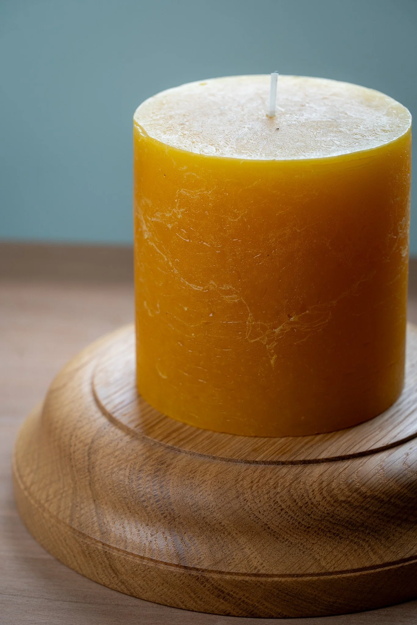 A large, cylindrical yellow candle with a white wick on a round wooden stand.