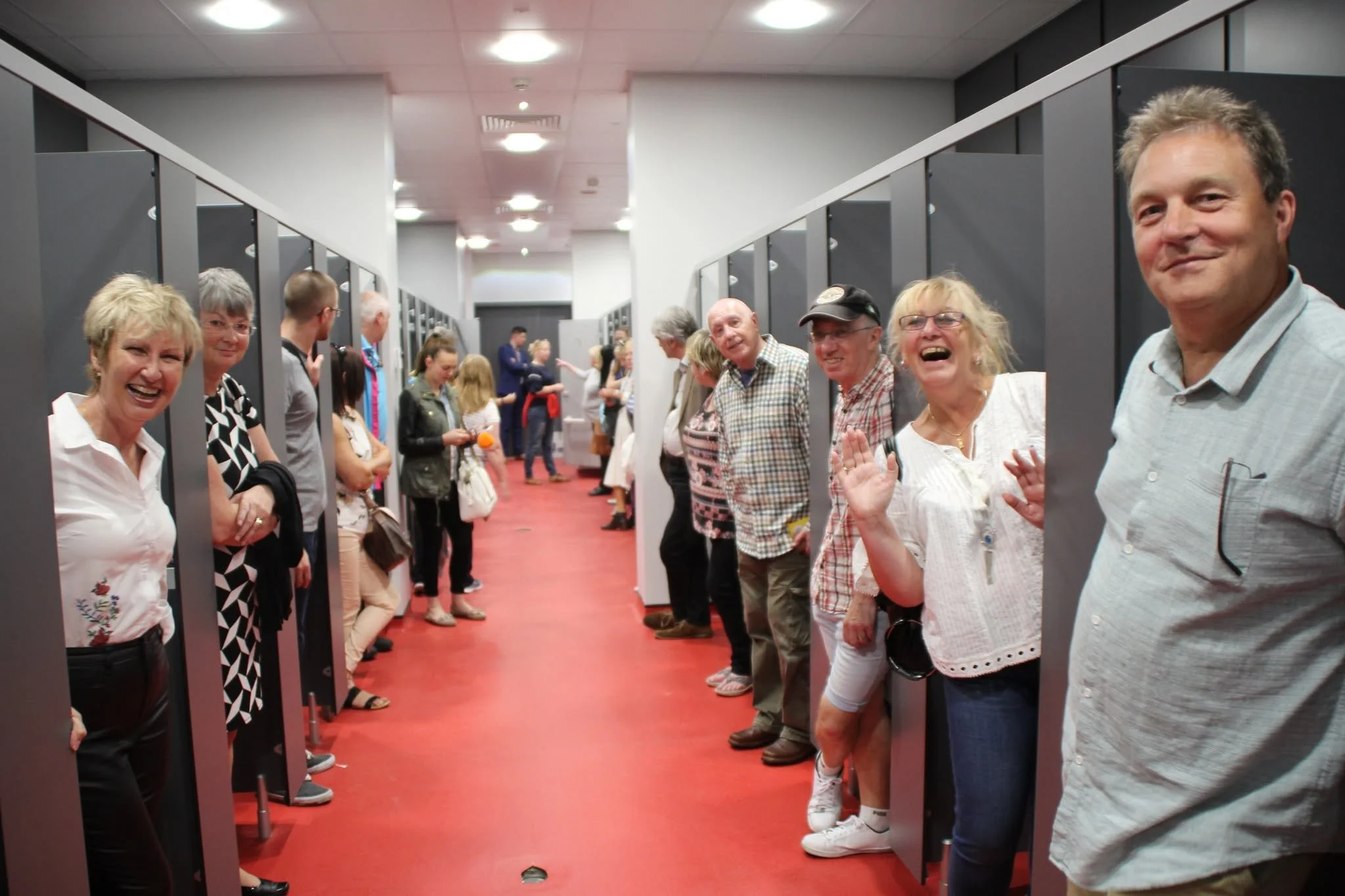 People standing in a line in a hallway with black lockers on each side, smiling and chatting.
