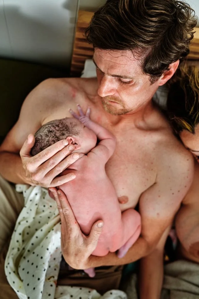 Birth photography in Austin, Texas by Breeanna Rose Photography. Vertical, dad holding baby to his chest.