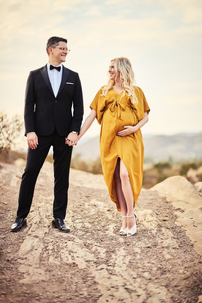 Maternity photography in Austin, Texas by Breeanna Rose Photography. Couple holding hands on rocky ground, mustard gown flowing, golden light.