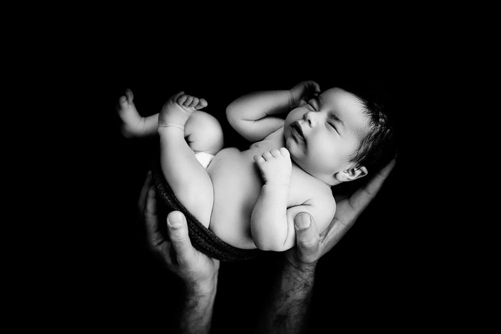Newborn photography in Austin, Texas by Breeanna Rose Photography. Black and white partner of the confirmed favorite, newborn held in hands against black.