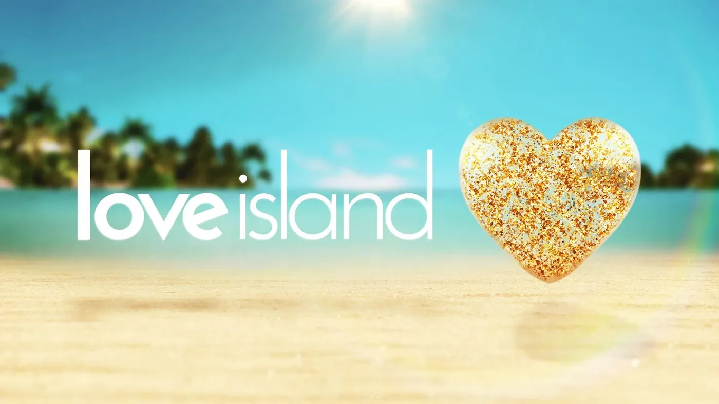 Beach scene with blue sky, turquoise water, distant trees, the words 'love island' in white font, and a gold glittery heart on the sandy shore.
