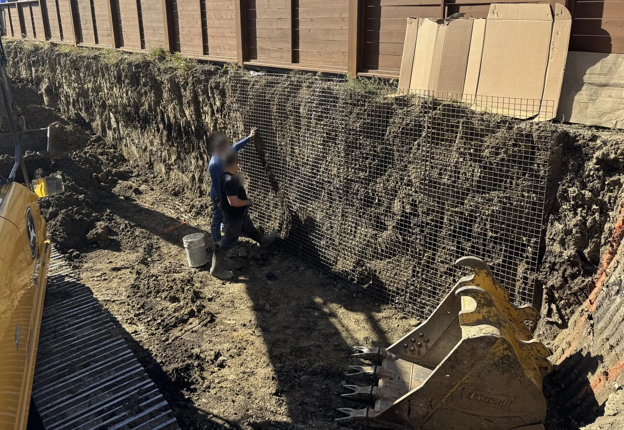 Welded wire mesh pinned to the excavation face before shotcrete, with a crew member securing the mesh