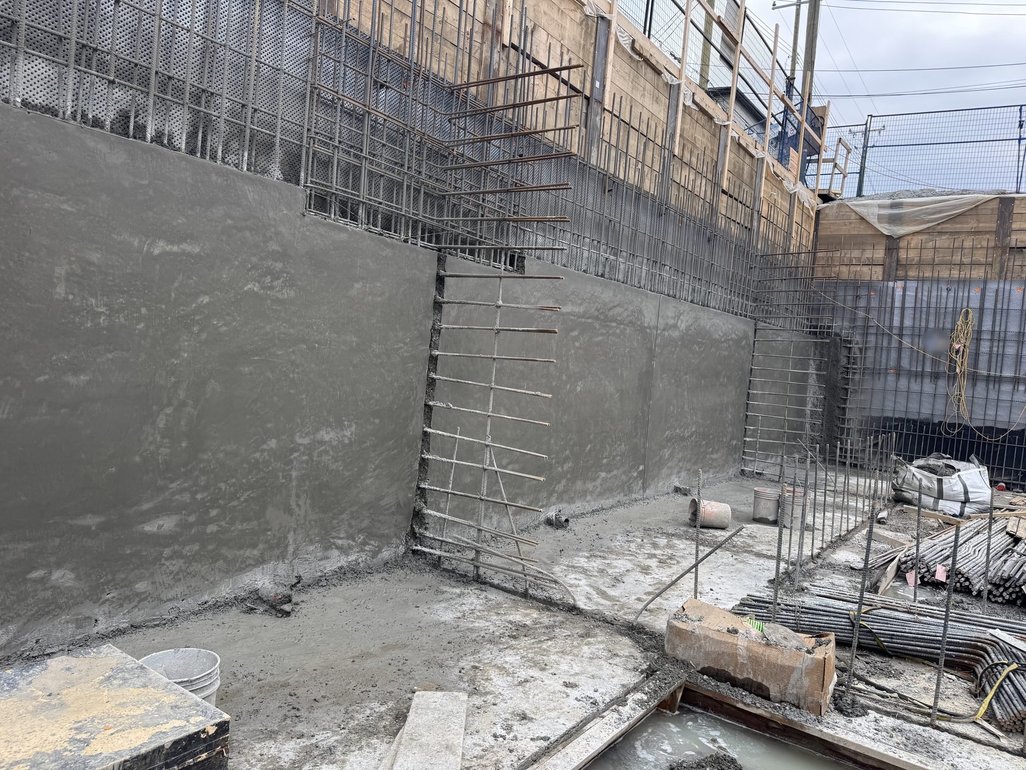 Finished structural shotcrete wall turning a corner in an Edmonton excavation, rebar mats over drainage board and timber shoring above