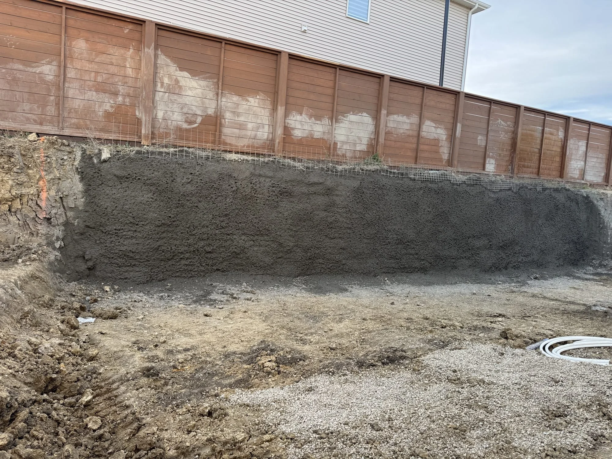 Finished temporary shotcrete shoring wall along a fenced property line in a residential basement excavation in Calgary