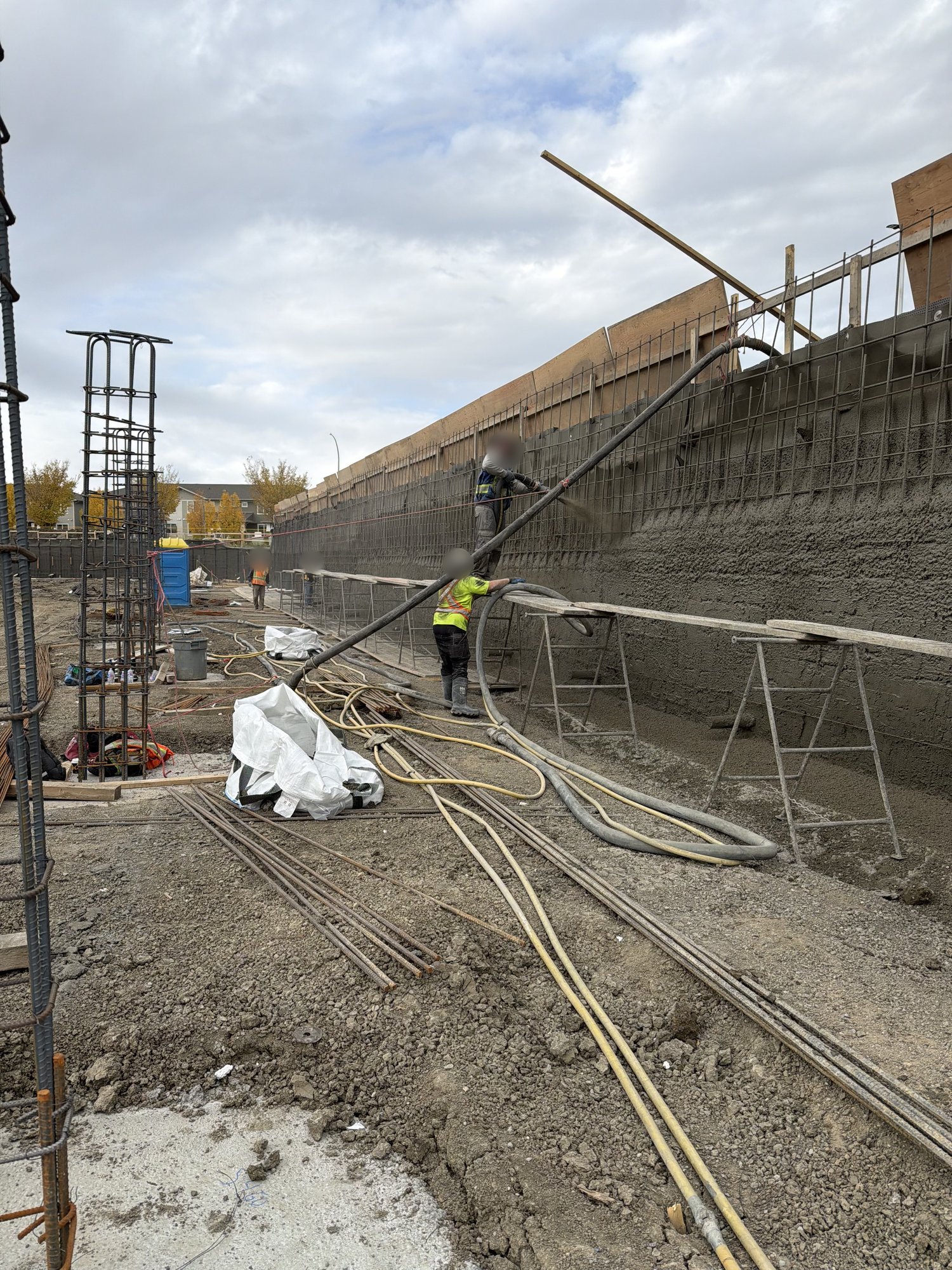 Shotcrete going onto a rebar mat along a shored excavation, crew on a scaffold walkway