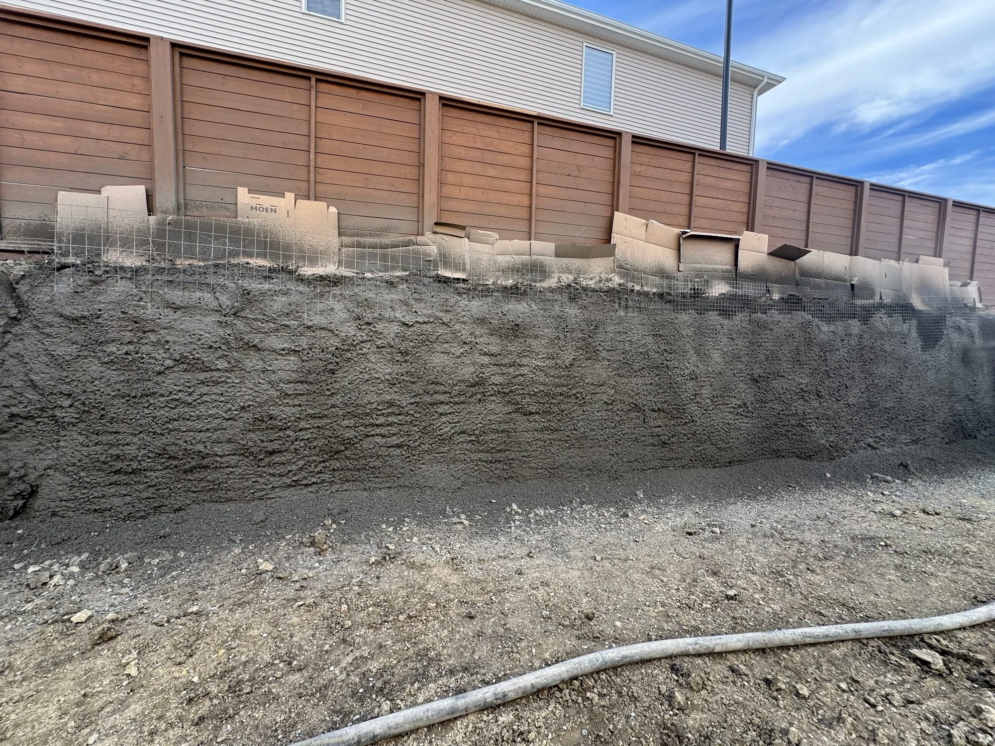 Freshly sprayed shotcrete face along a residential excavation, with cardboard protecting the base of the neighbouring fence
