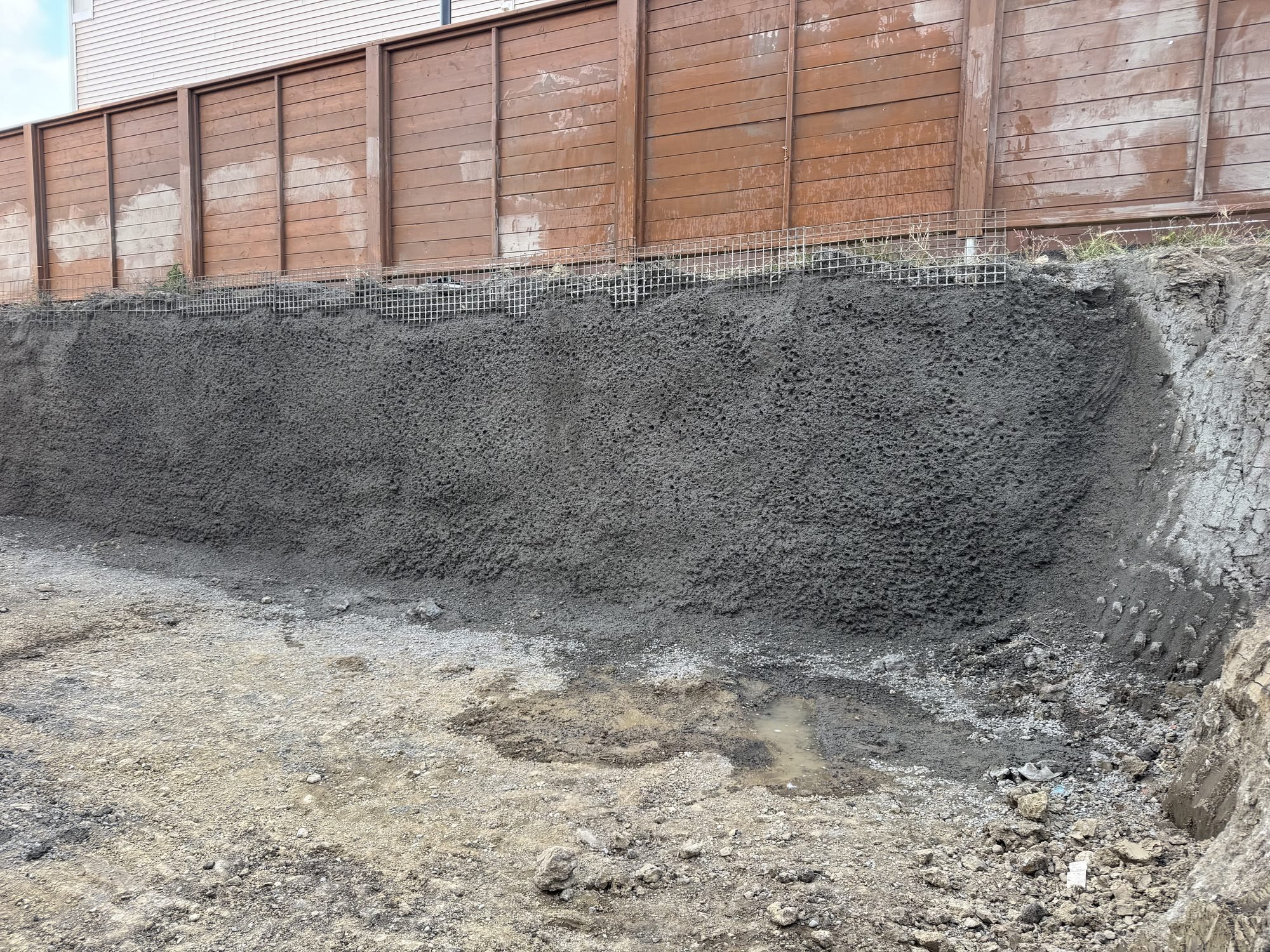 Finished temporary shotcrete shoring wall below a wooden fence line in a residential basement excavation