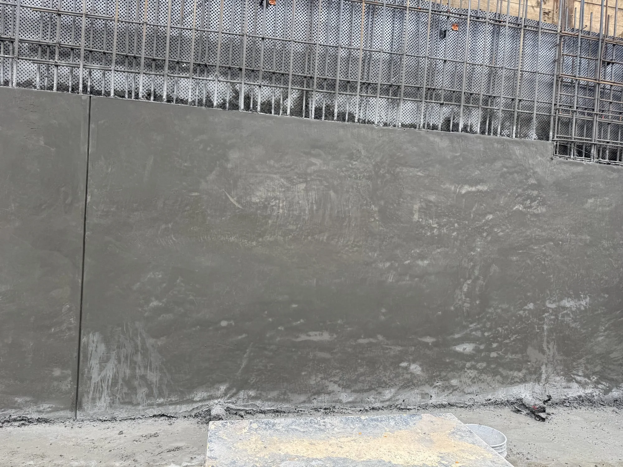 Straight-on view of a finished structural shotcrete wall with a vertical joint, rebar mat over drainage board above