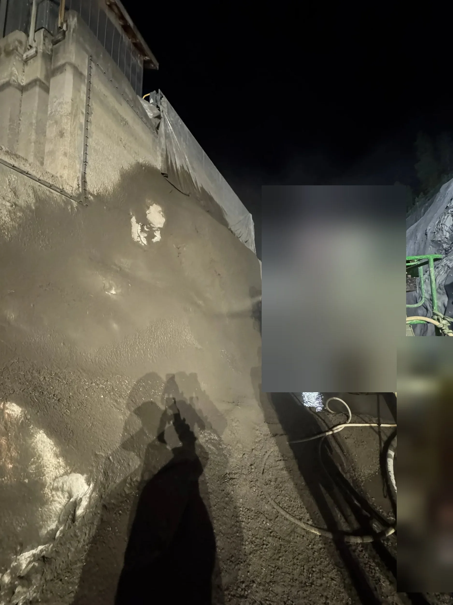 Freshly sprayed shotcrete wall under site lighting at night