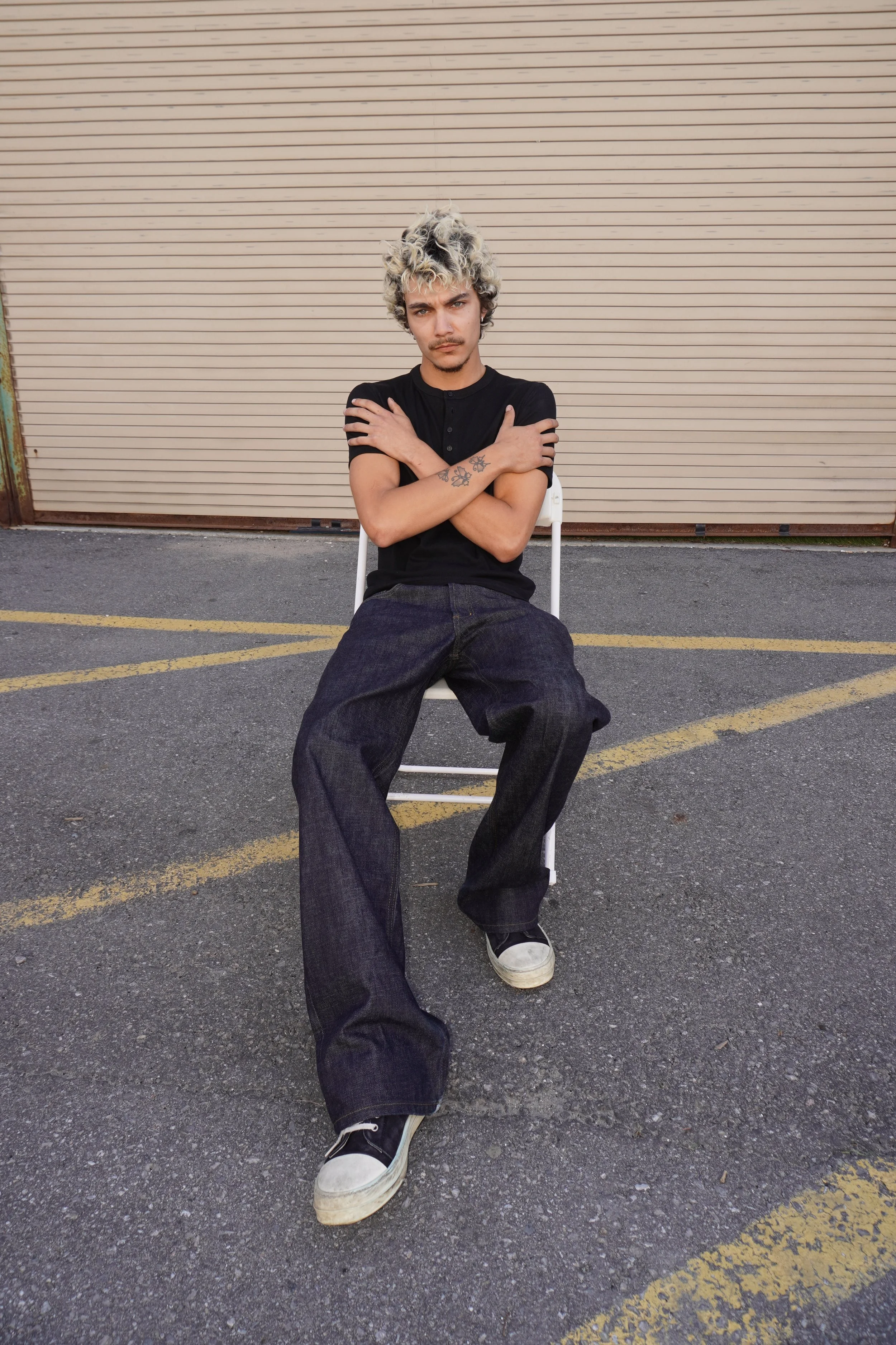 Quinton, male fashion model represented by Noirvelle Models, seated outdoors in a black T-shirt and dark jeans.