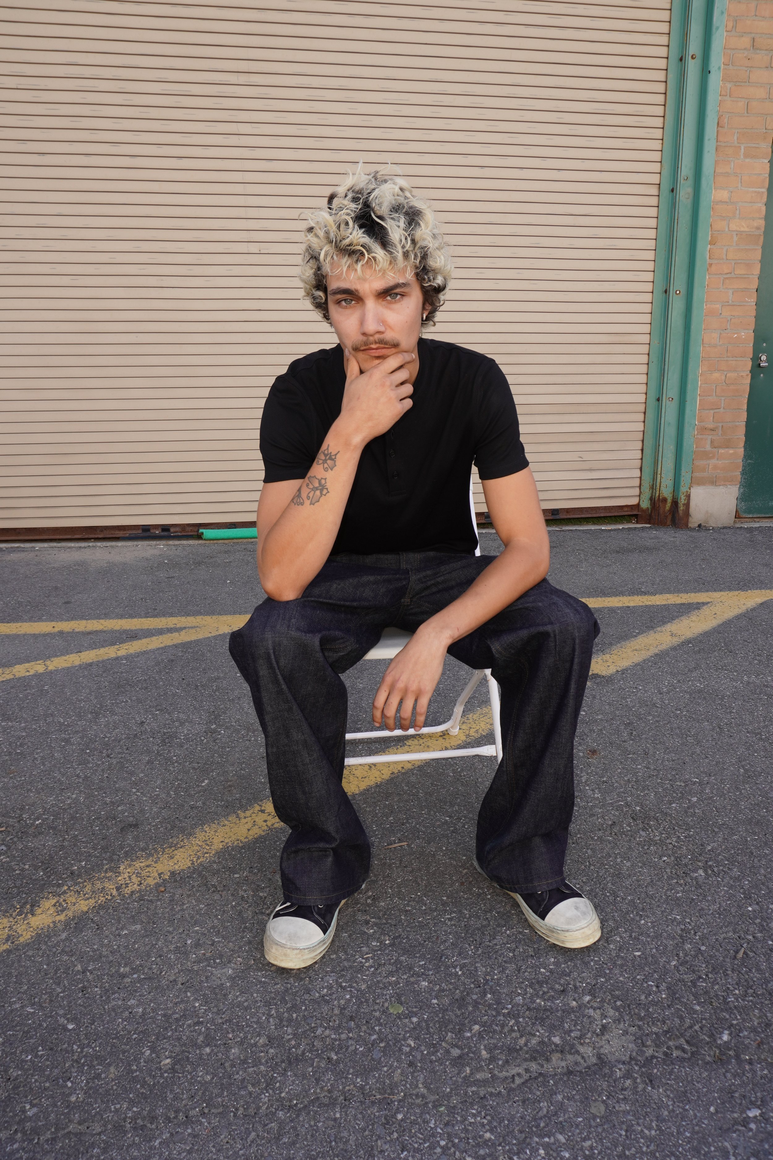 Quinton, male fashion model represented by Noirvelle Models, posing outdoors in a black T-shirt and dark jeans.

