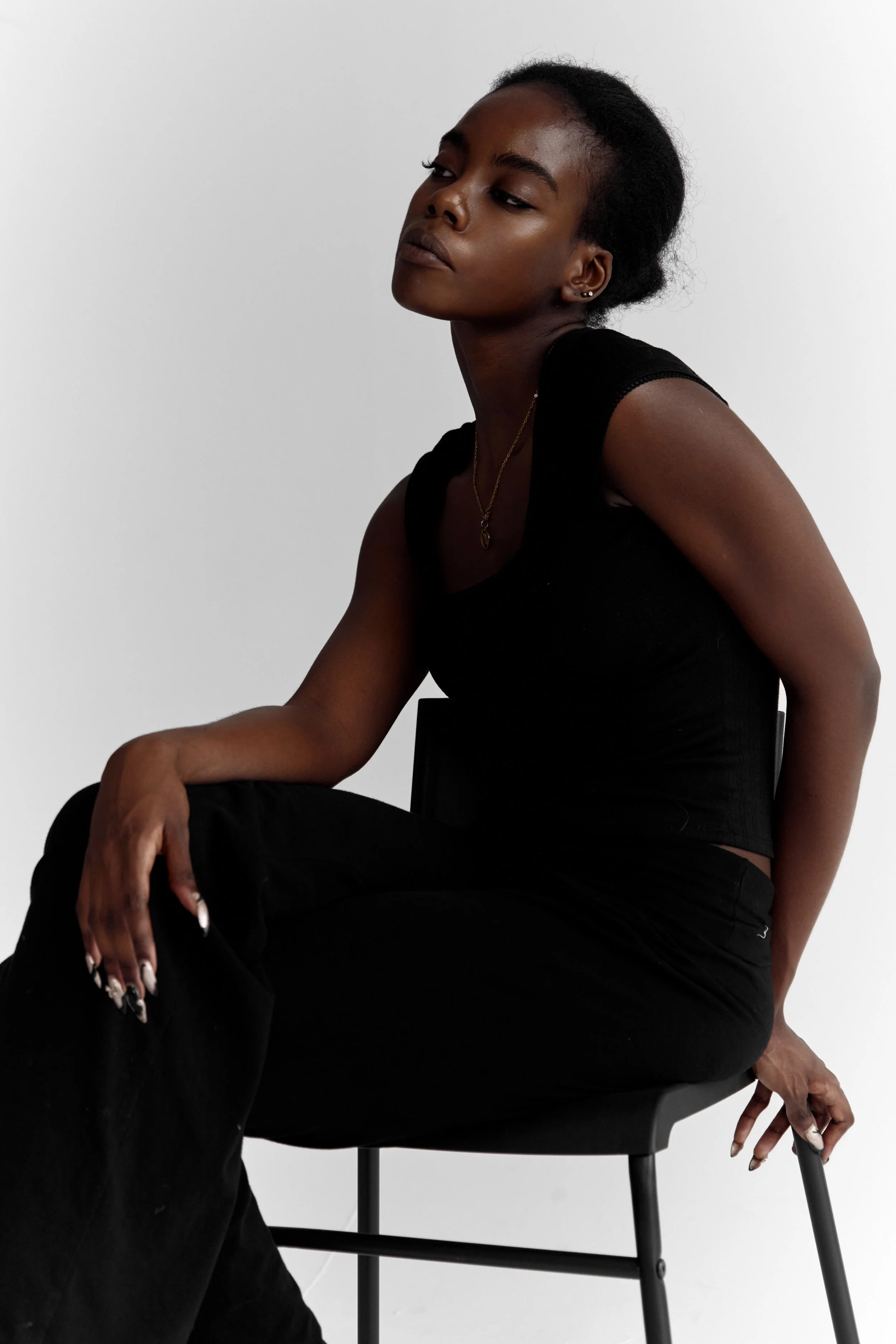 Daisy — female fashion model represented by Noirvelle Models, seated on a black chair in a minimalist fashion portrait.
