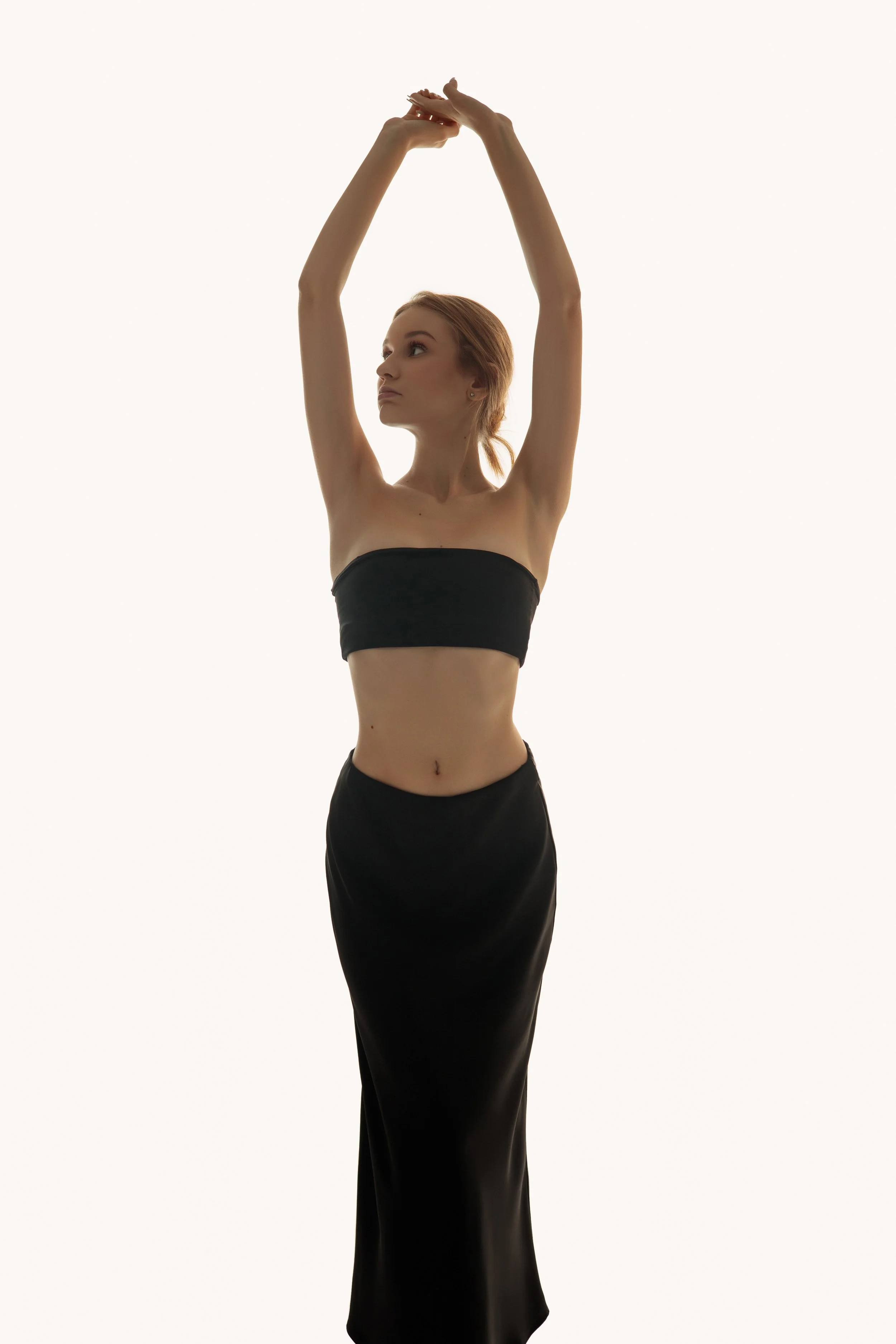 Victoria, female model represented by Noirvelle Models, posing in a black top and long black skirt against a white studio background.
