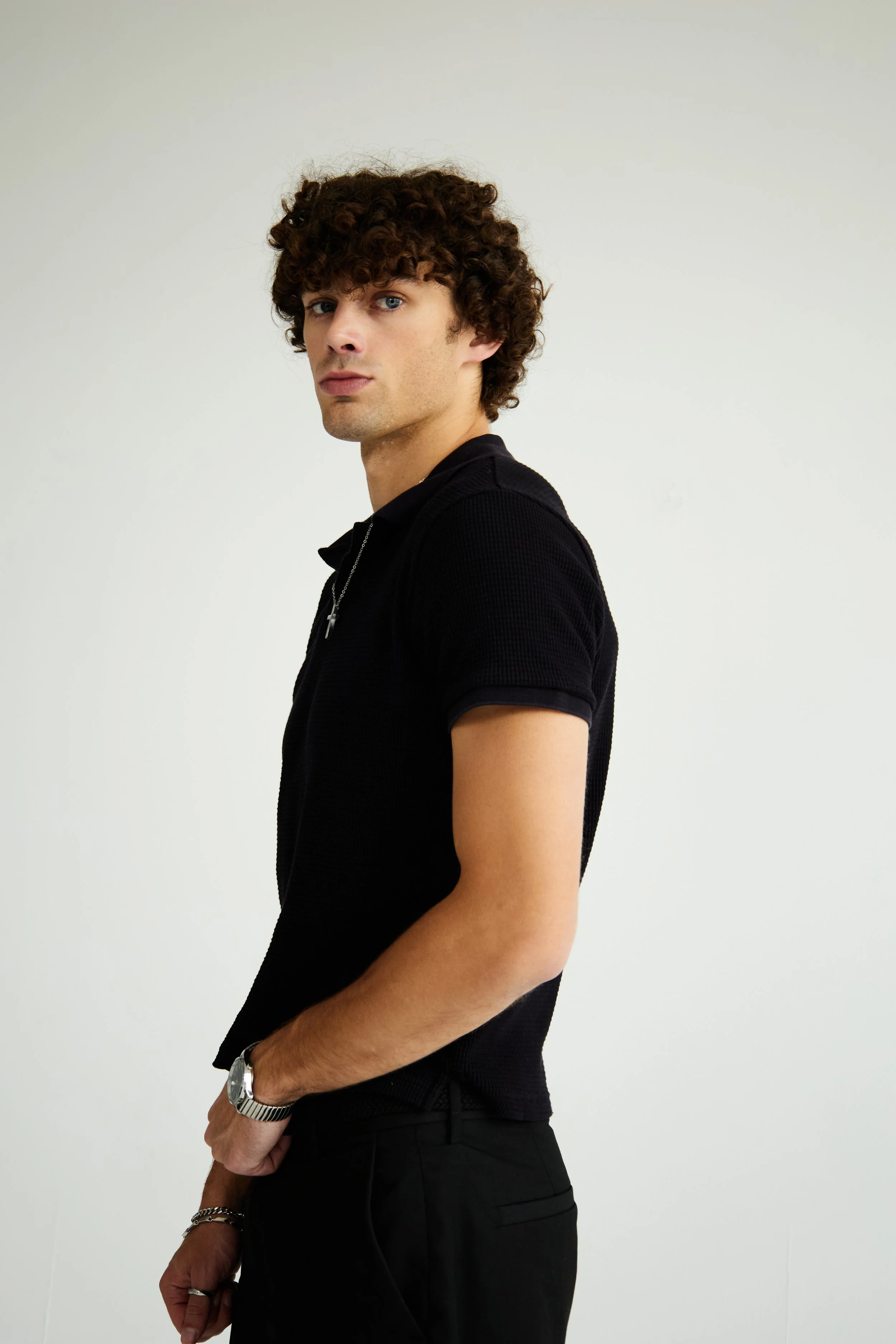 Maverick, male fashion model represented by Noirvelle Models, posing in profile in an all-black look against a white studio background.
