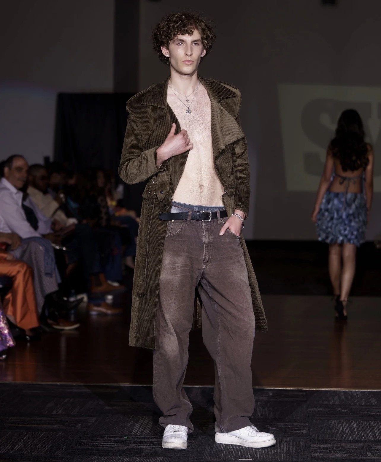 Andrea, male fashion model represented by Noirvelle Models, walking the runway in a brown corduroy outfit during a fashion show.
