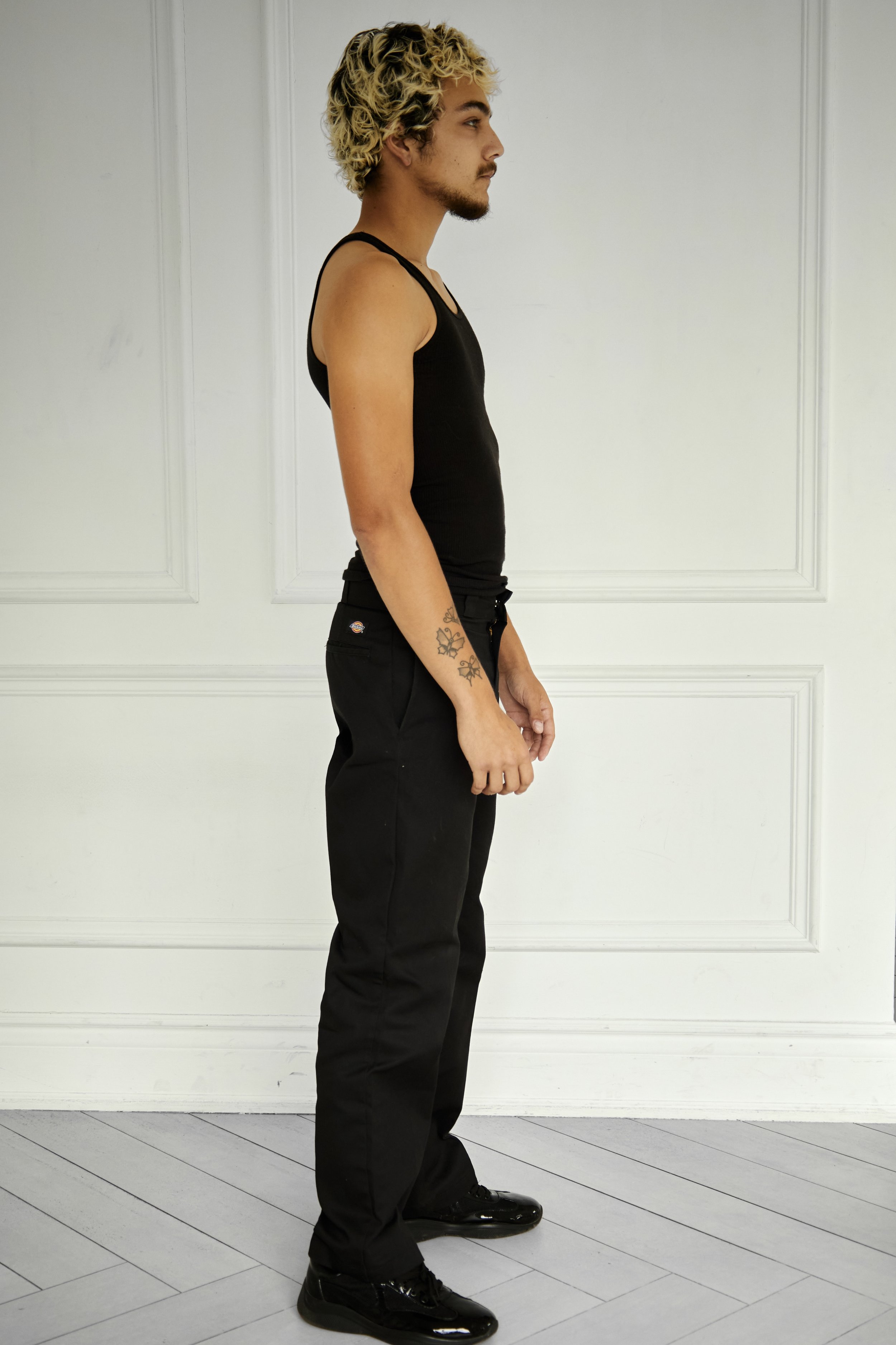 Quinton, male fashion model represented by Noirvelle Models, full-length side profile in black clothing against a white studio background.