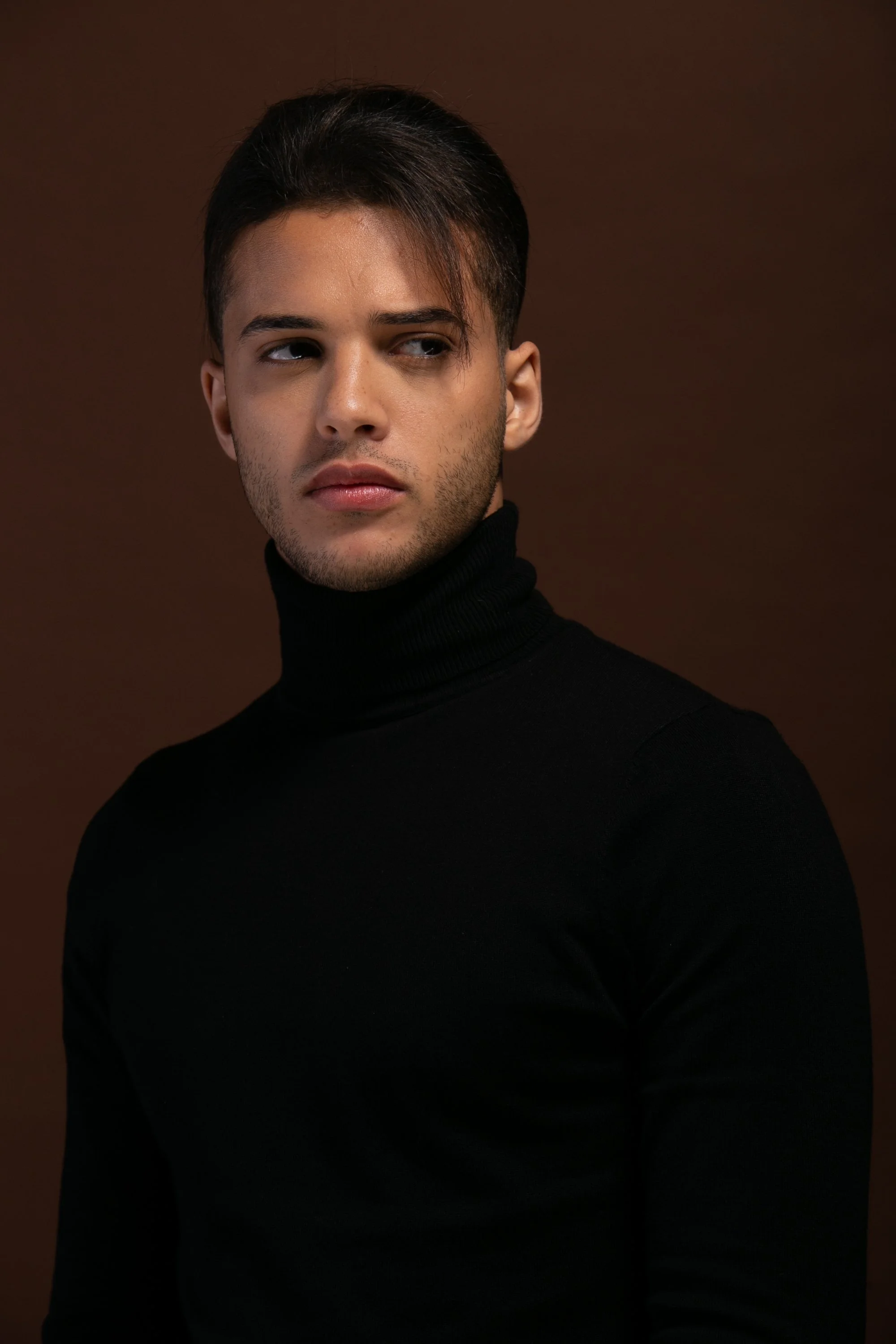  Bashir, male fashion model represented by Noirvelle Models, wearing a black turtleneck in a dark studio portrait.
