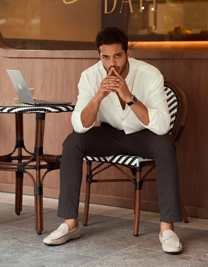 Bashir, male model represented by Noirvelle Models, seated in a white shirt during a lifestyle editorial photoshoot.
