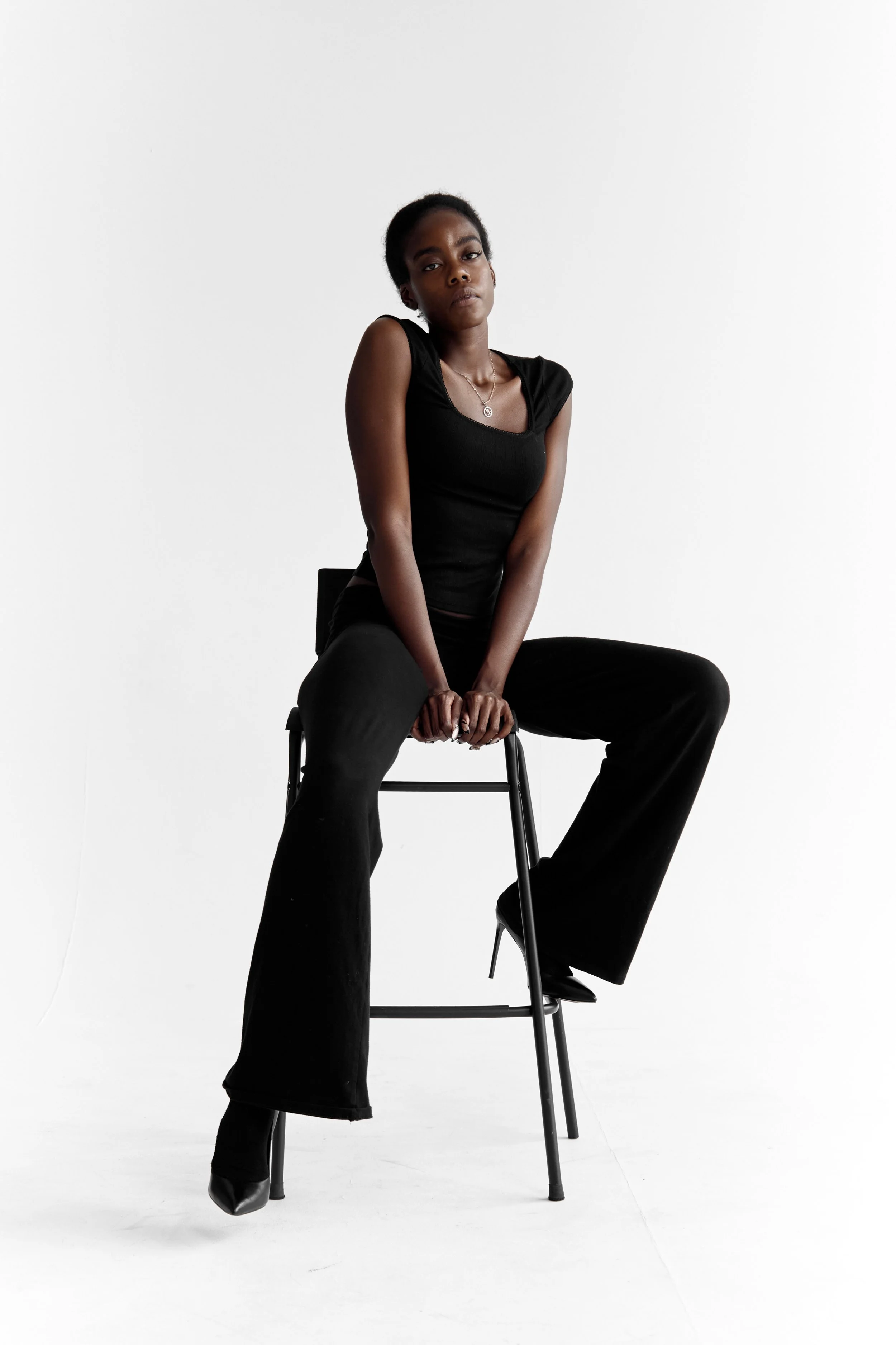 Daisy, female fashion model represented by Noirvelle Models, seated in a black outfit against a white studio background.
