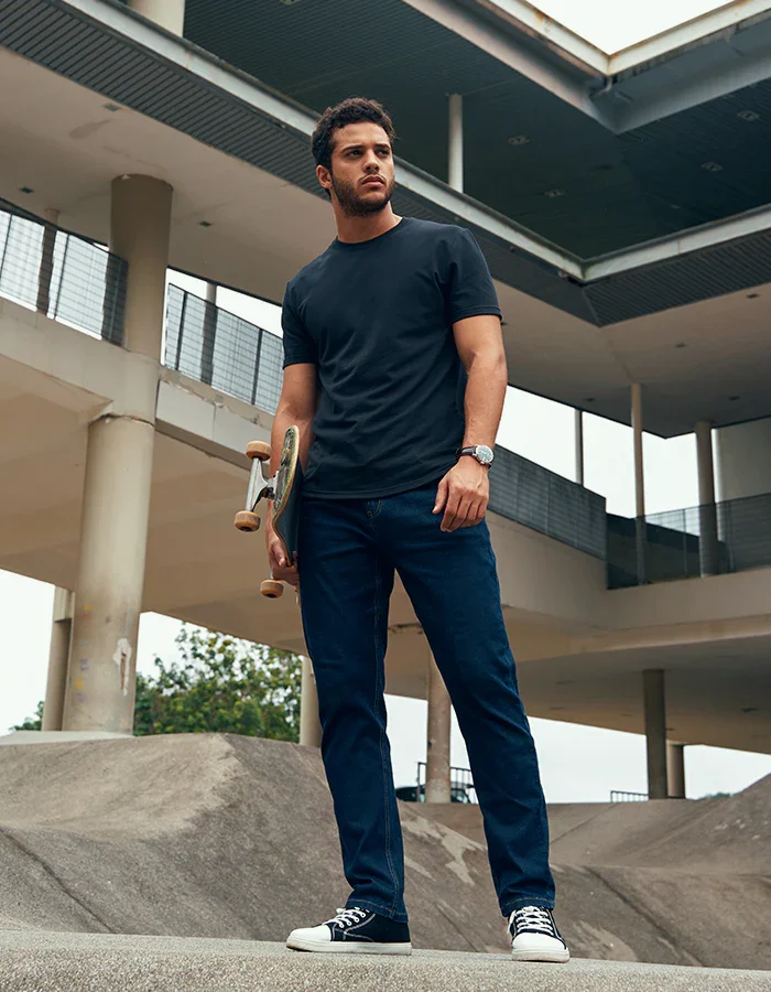 Bashir, male fashion model represented by Noirvelle Models, posing outdoors with a skateboard in a contemporary urban setting.
