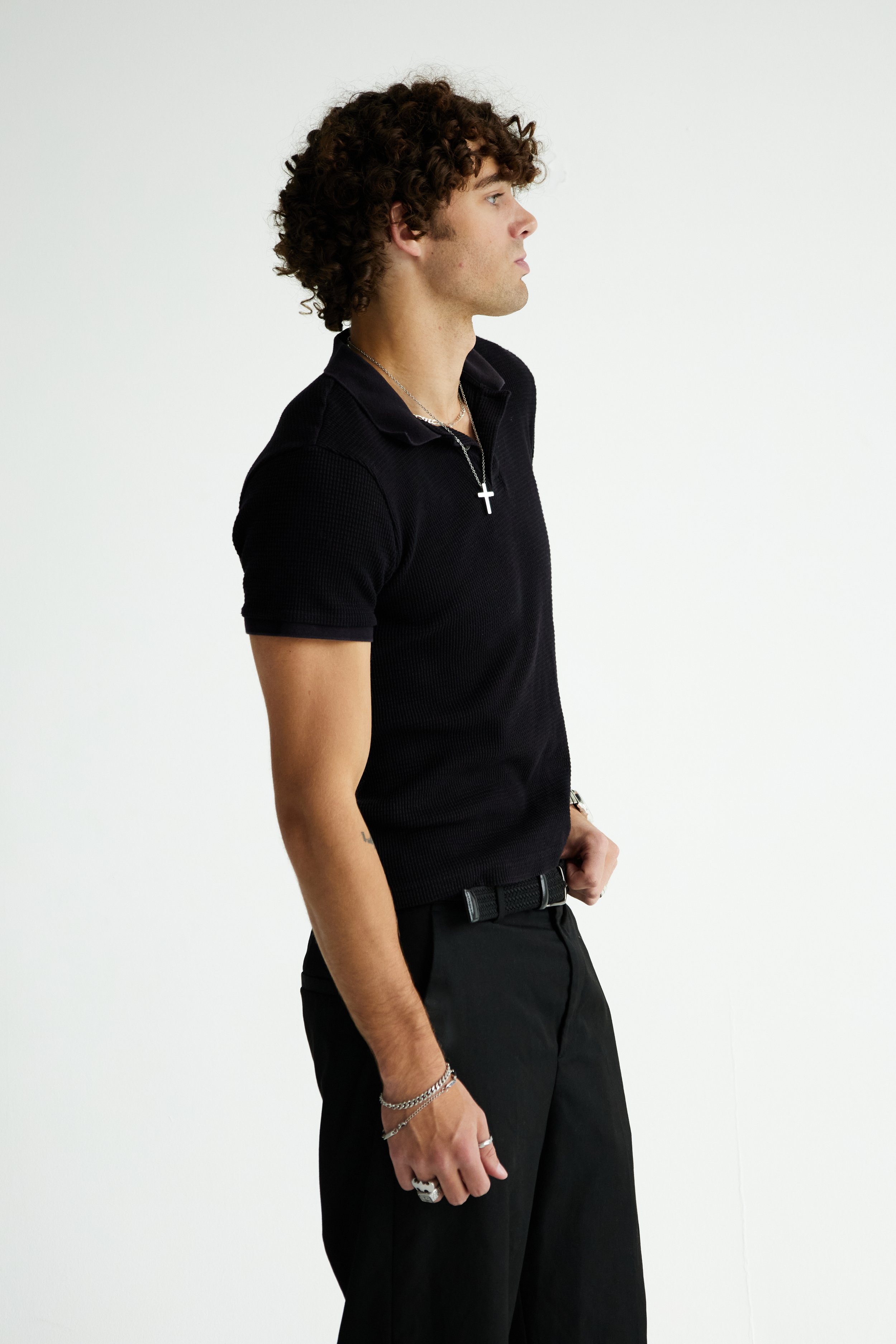 Maverick, male fashion model represented by Noirvelle Models, posing in profile in an all-black look against a white studio background.
